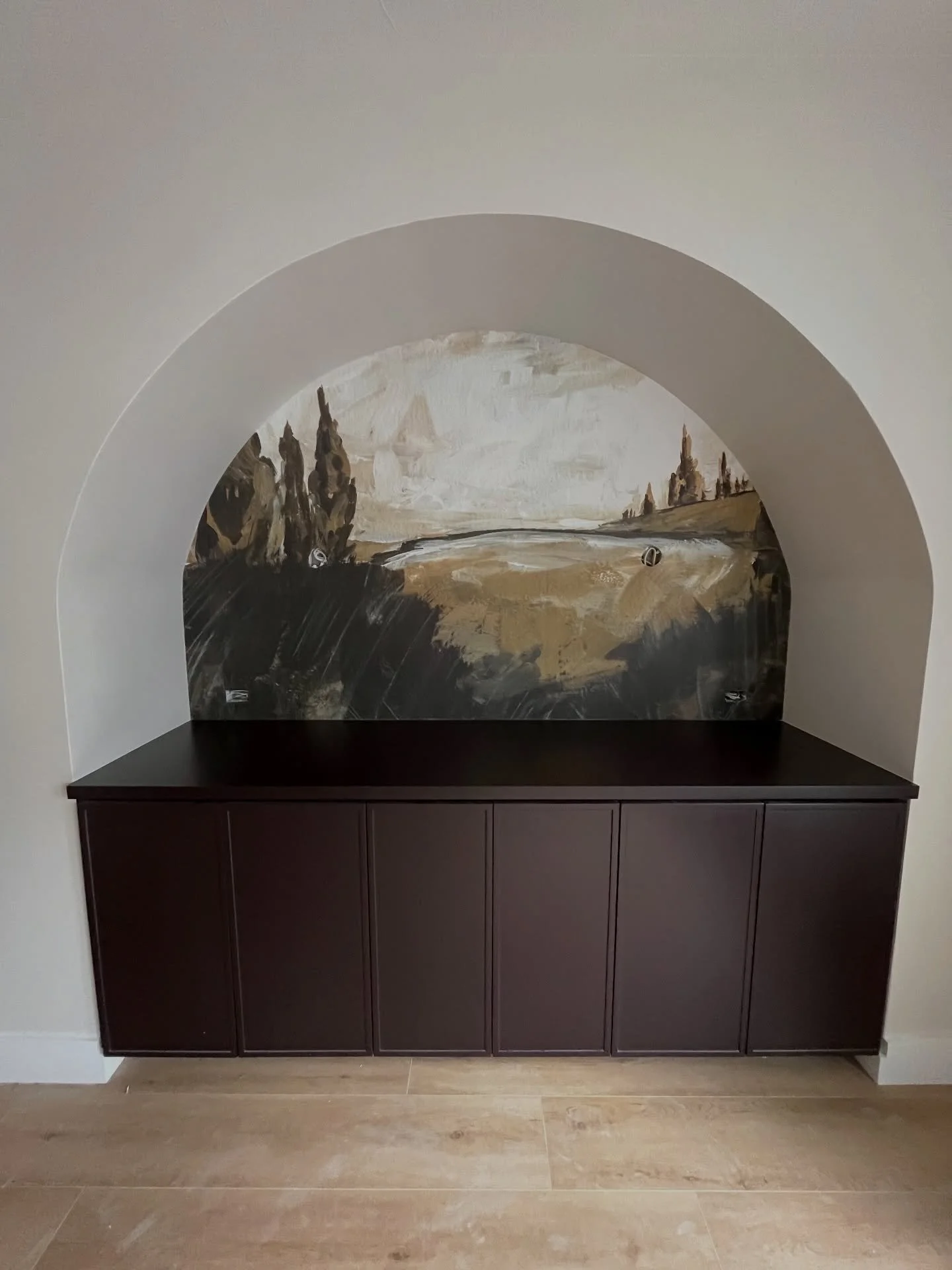 MOOD | This dining room transformation is one of those spaces that instantly sets the tone. We removed the outdated columns and designed a custom arched alcove to frame our client&rsquo;s buffet in a rich, deep wine hue; then layered in a mural that 