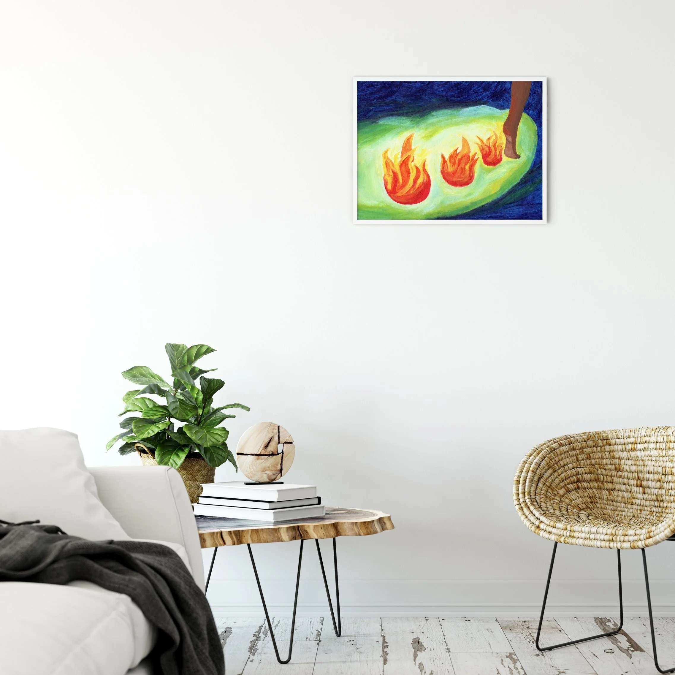 Living room with a white wall, a colorful abstract painting of flames and a foot on the wall, a green potted plant, a round wooden sculpture, stacked books, a wicker chair, and a white sofa with a dark blanket.