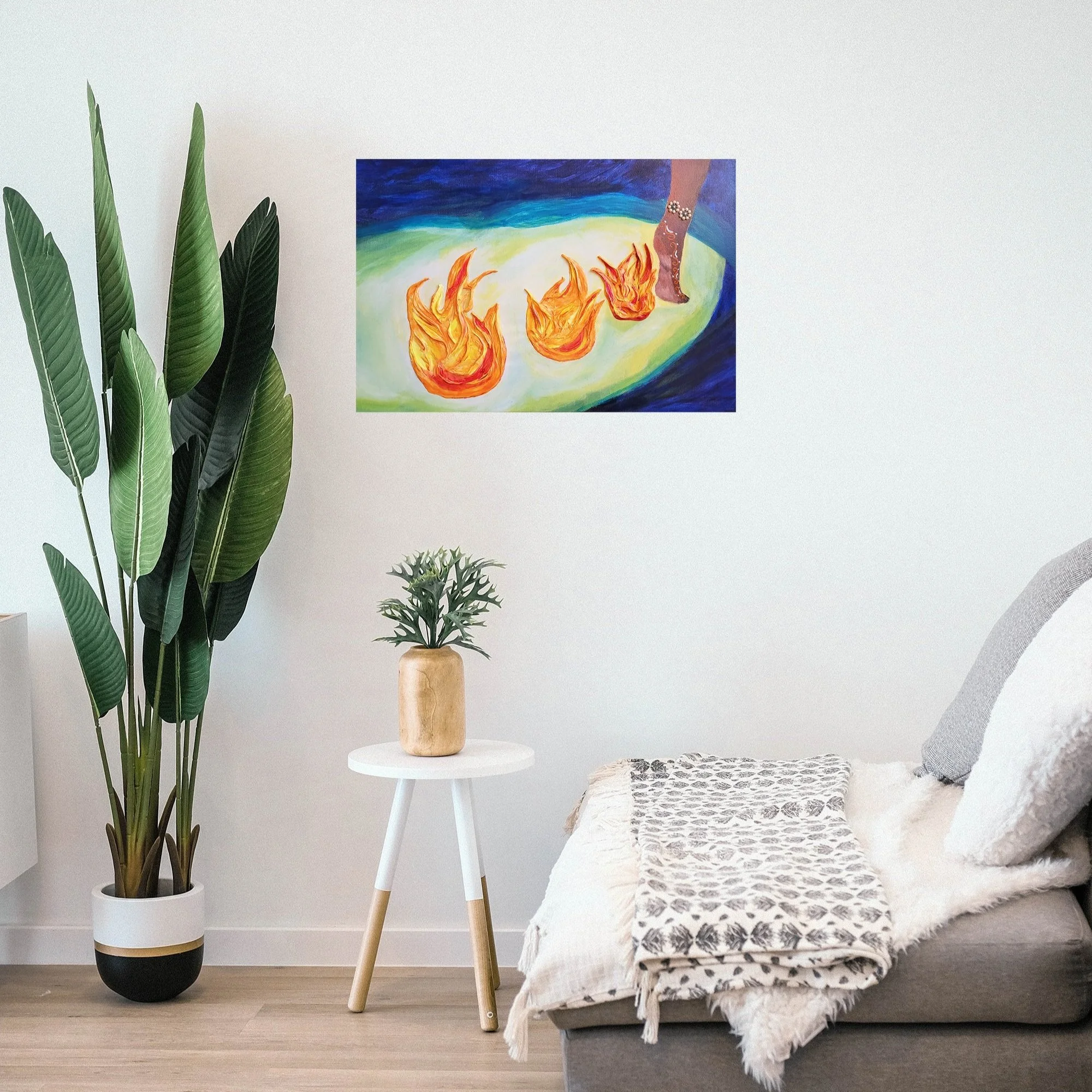 A modern living room with a large potted plant on the left, a small side table with a plant in a wooden pot, a bed with a patterned blanket and pillows on the right, and a colorful abstract painting on the wall above, depicting flames and a foot adorned with jewelry.
