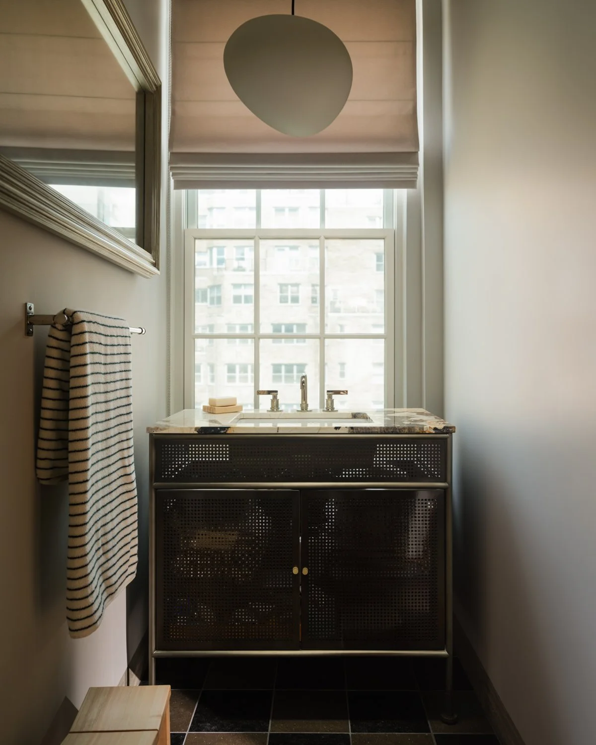 Small bathroom with a window, marble sink, black and white striped towel, and black tiled floor.