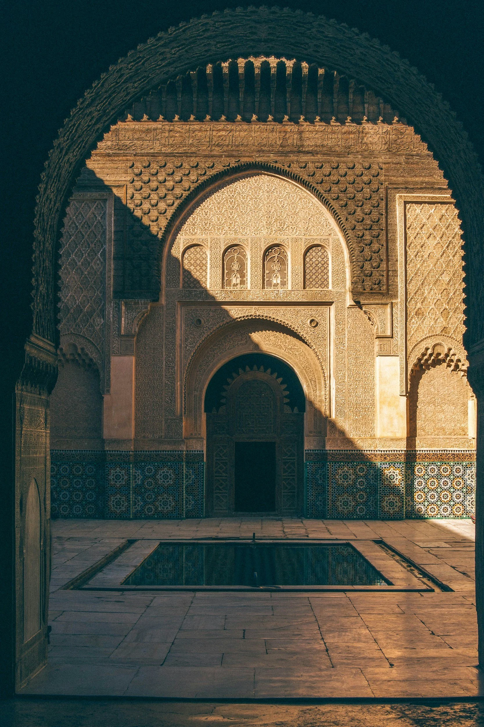 Interior view of a Moroccan-style courtyard with ornate archways, intricate tile work, and a small reflecting pool.