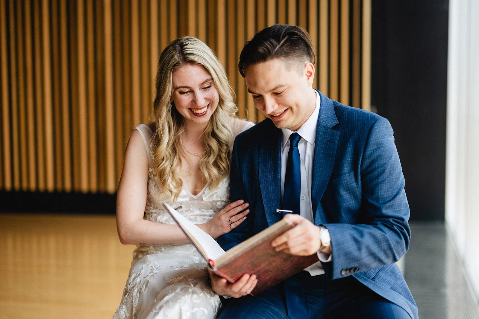 A happy couple dressed in formal attire looking at a book together indoors.