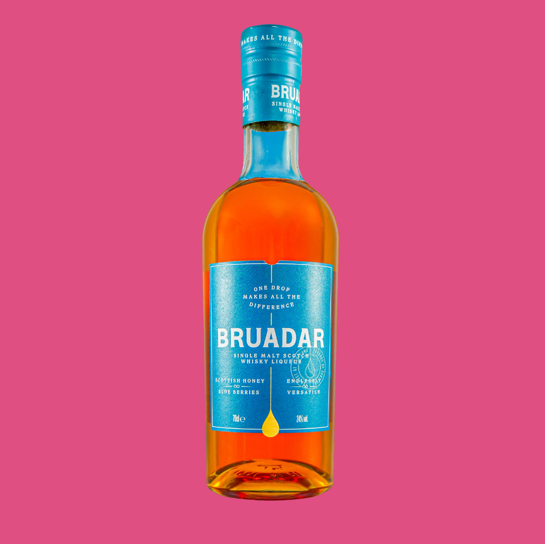 A bottle of Bruadar single malt Scotch whisky with a blue label, orange liquid inside, against a pink background.