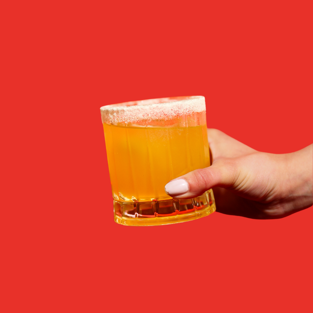 A hand holding a margarita cocktail against a red background.