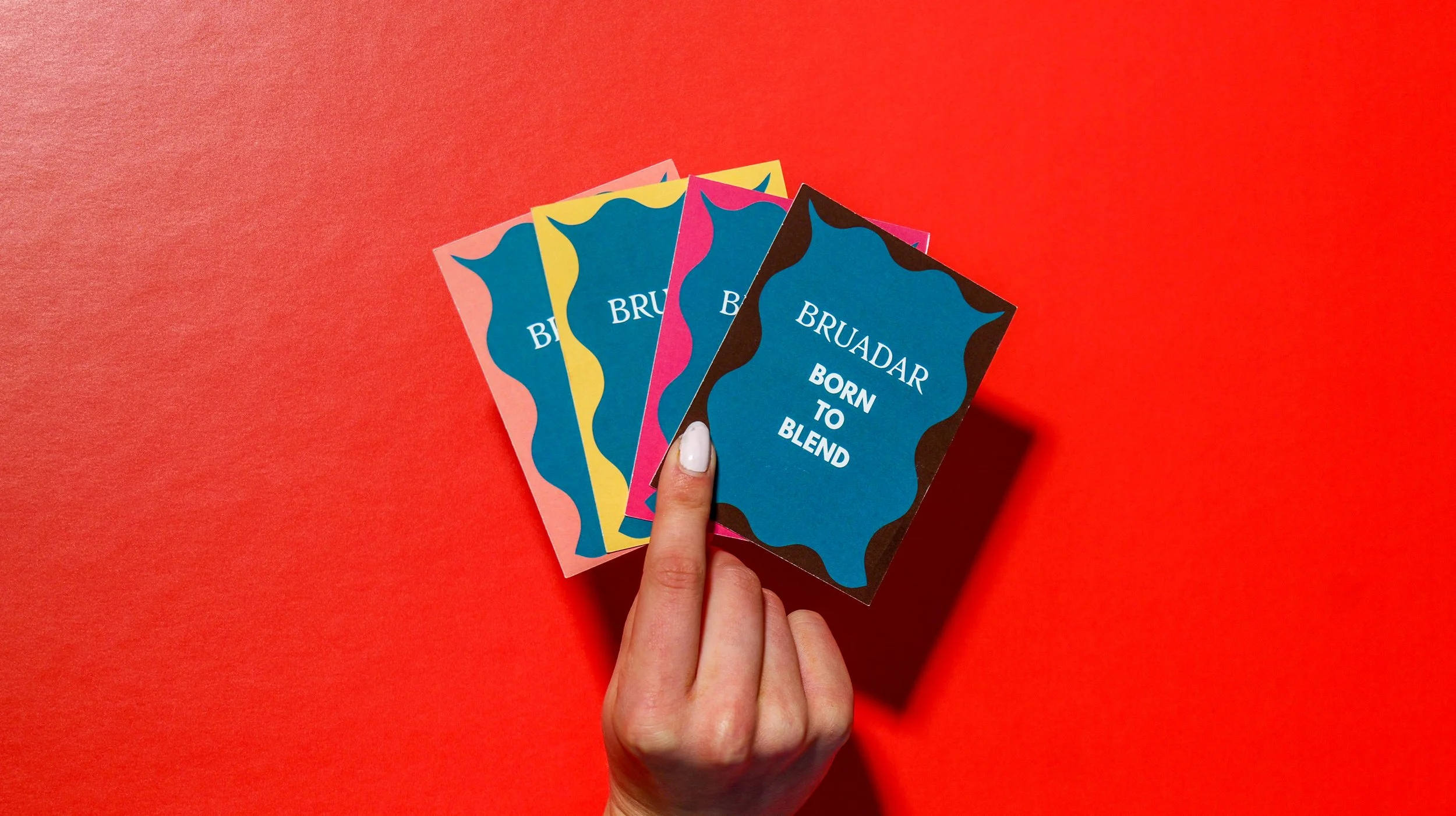 Person holding four colorful cards with the words "Bruadar Born to Blend" on a red background.