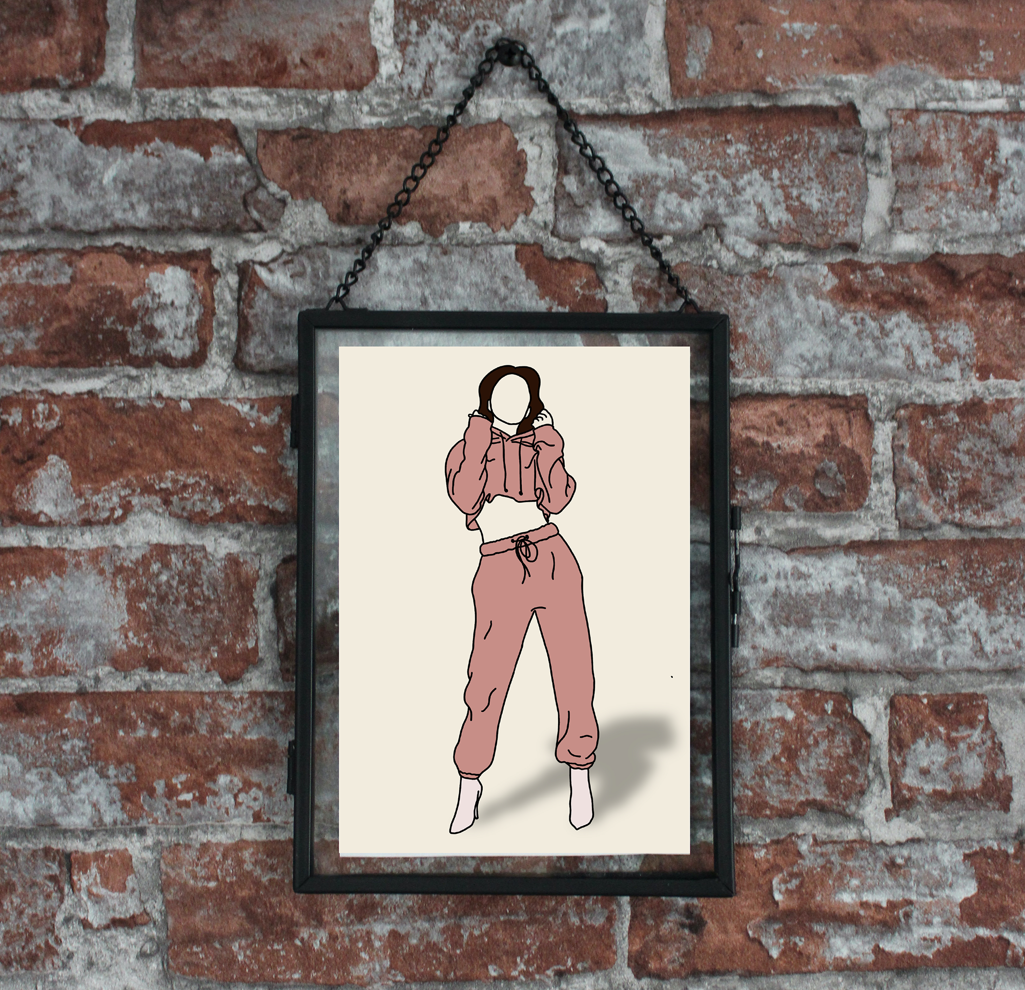 A framed digital illustration of a faceless woman in a pink hoodie and matching pants, standing with one leg slightly bent, displayed on a brick wall.