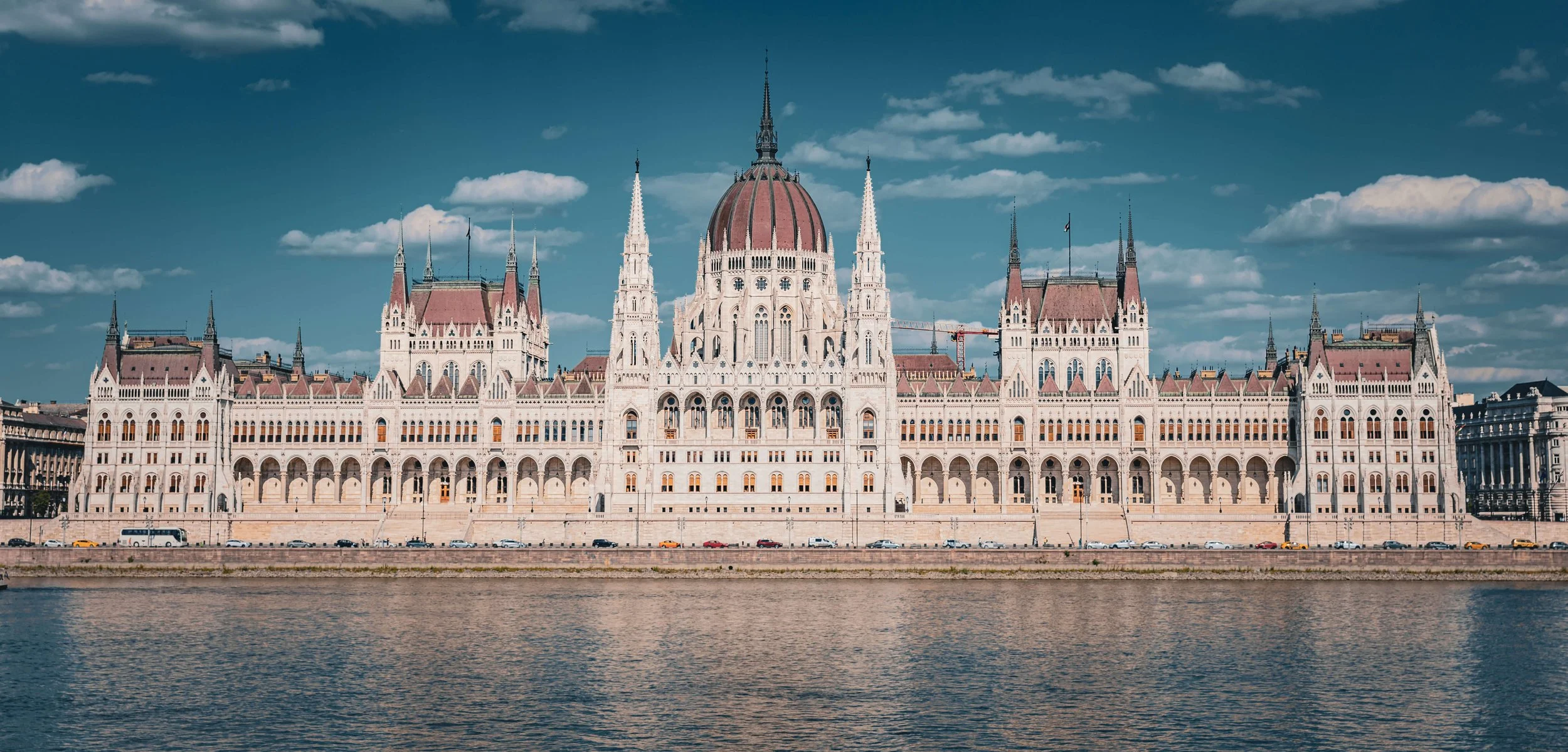The Hungarian Parliament Building in Budapest, seen from across the Danube River, with partly cloudy sky.