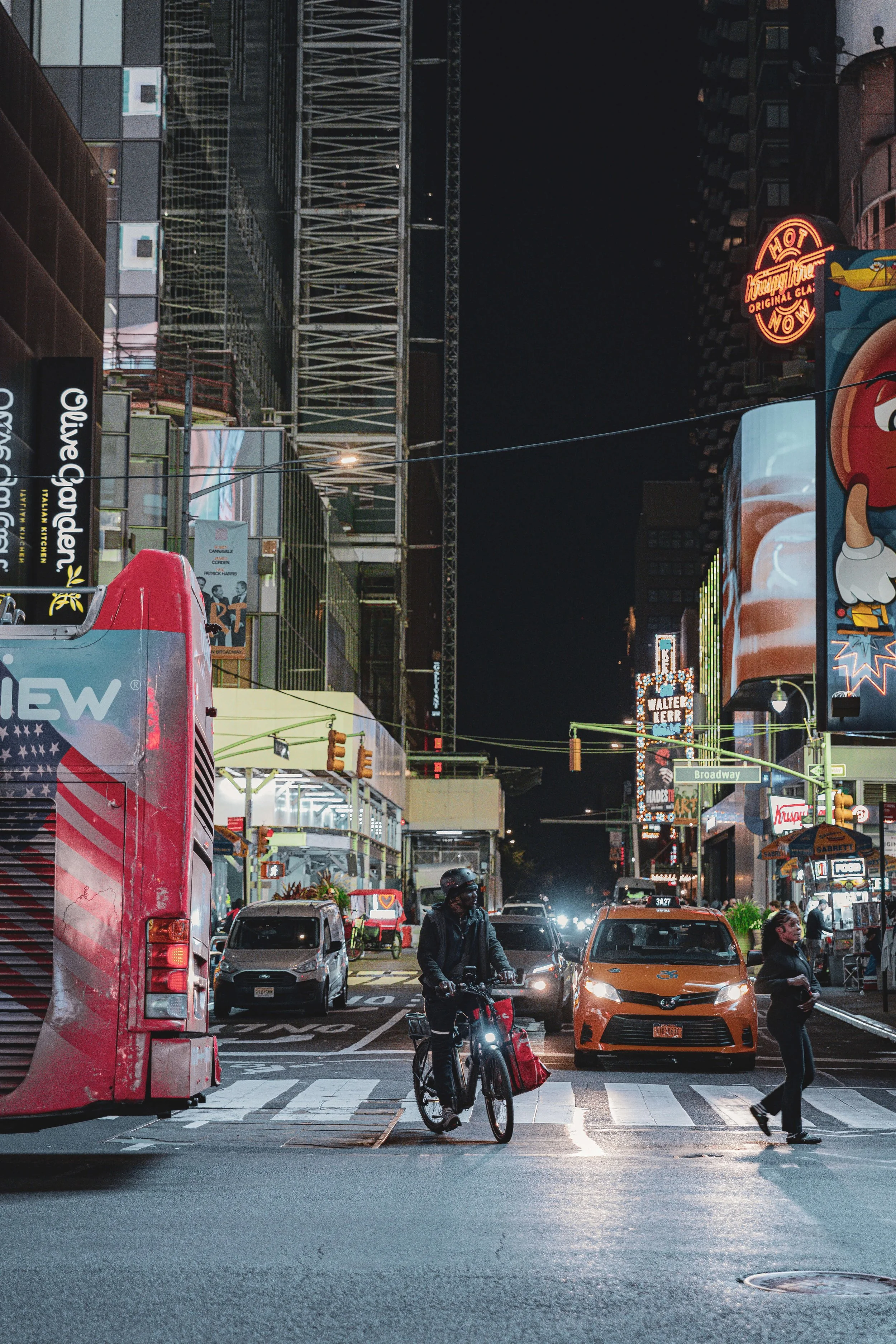 Nighttime city street scene with cars, taxis, pedestrians, billboards, and bright neon signs.