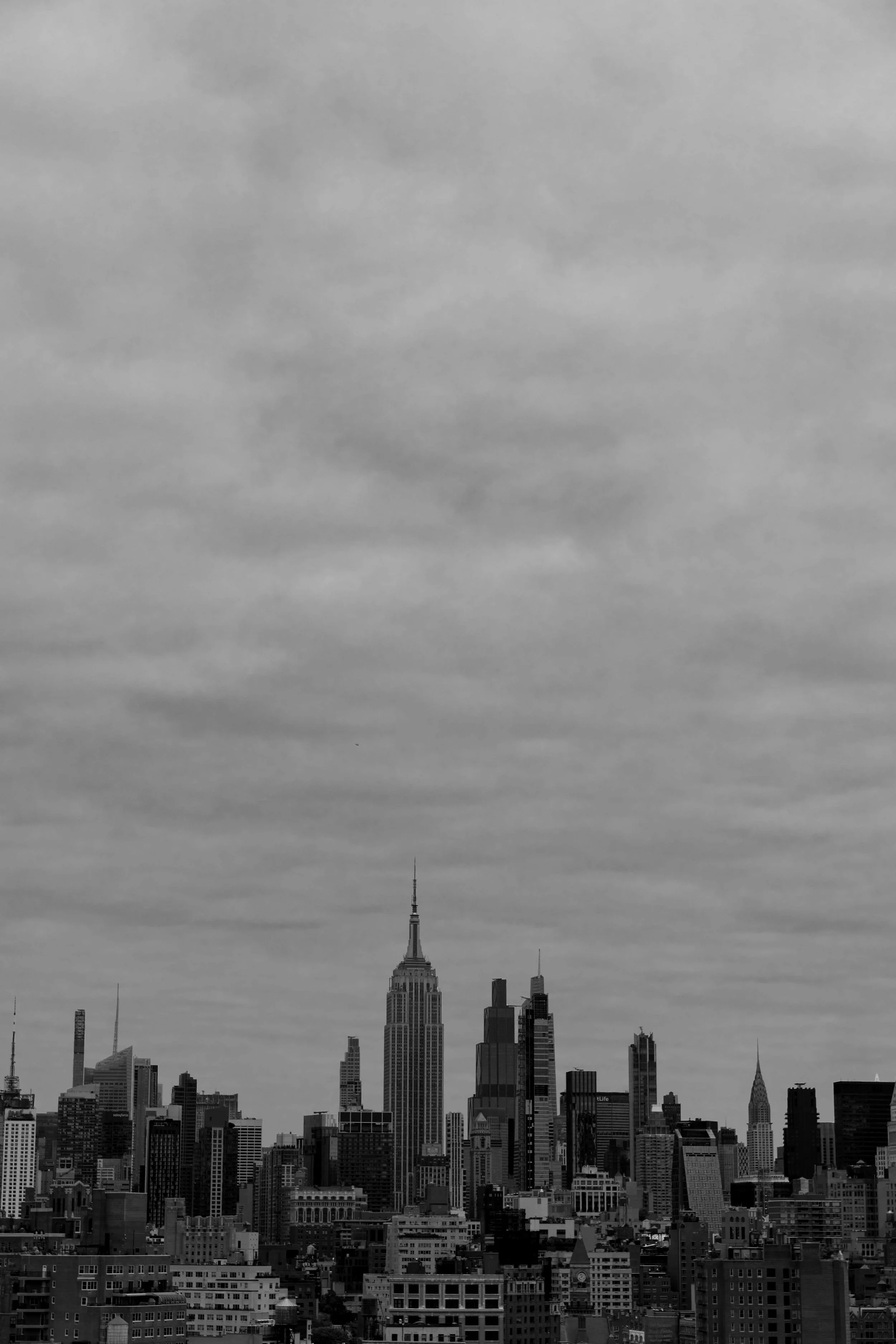 Black and white photo of the New York City skyline with the Empire State Building and other skyscrapers under a cloudy sky.