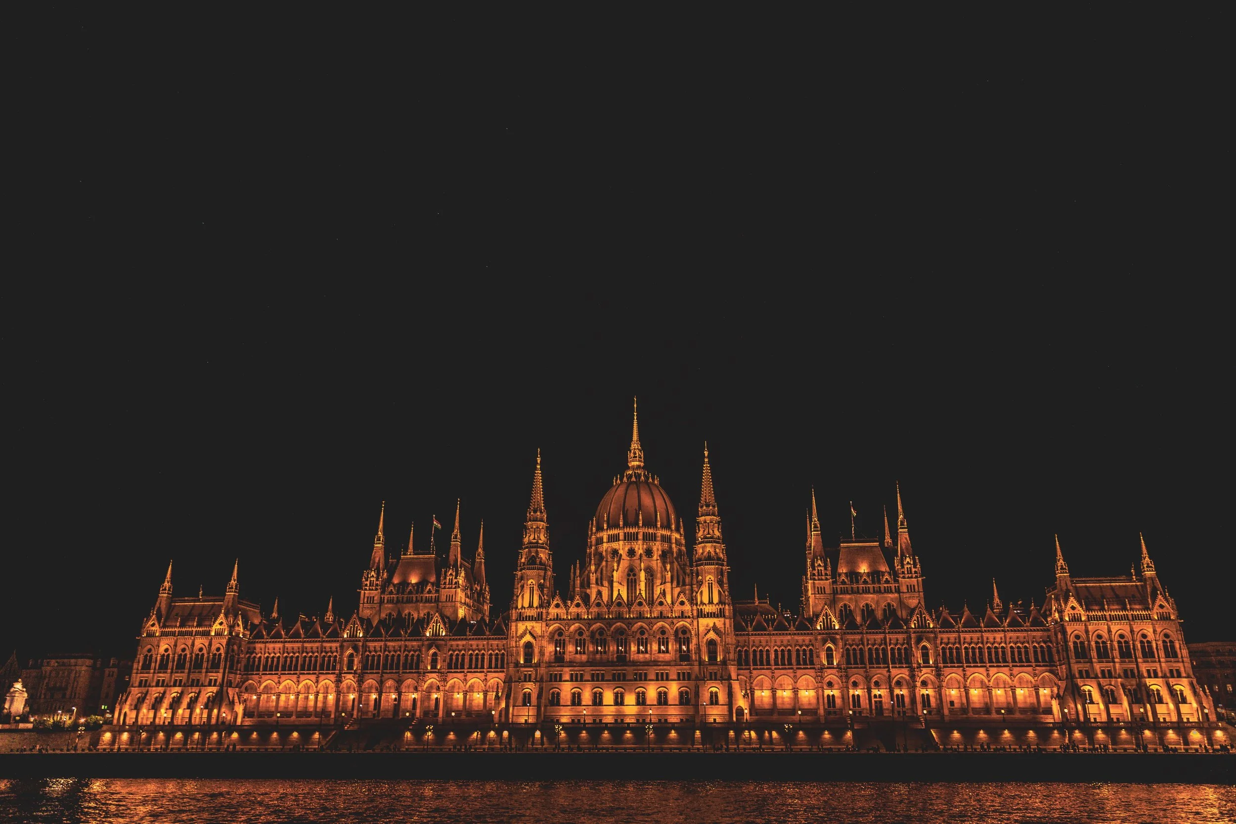Night view of the illuminated Hungarian Parliament Building with a dark sky and water reflection.