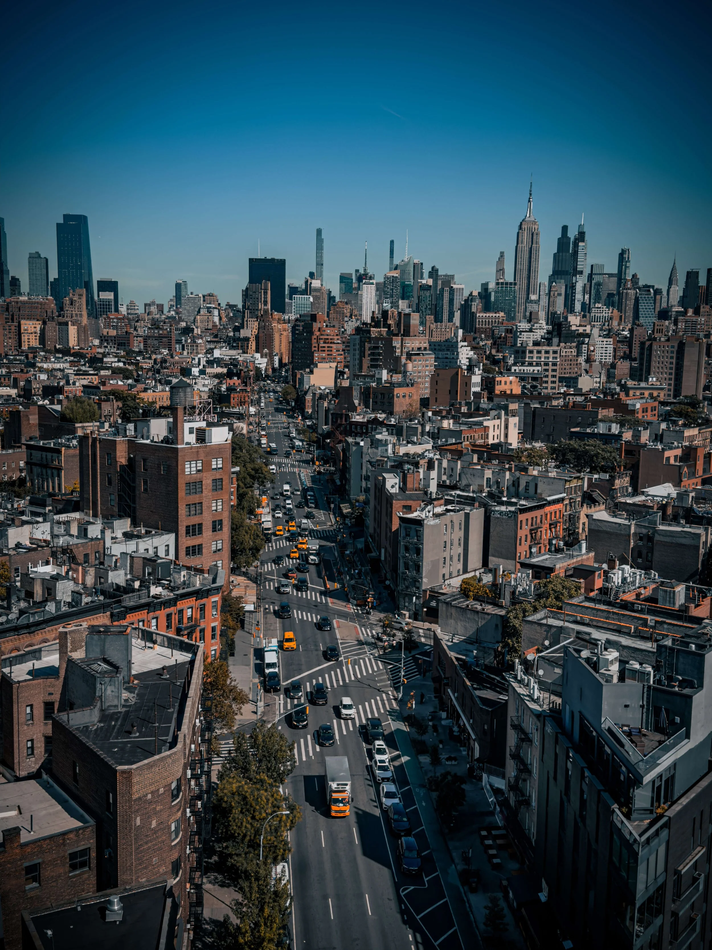 Aerial view of New York City skyline with tall skyscrapers including the Empire State Building, and busy streets with cars and taxis.
