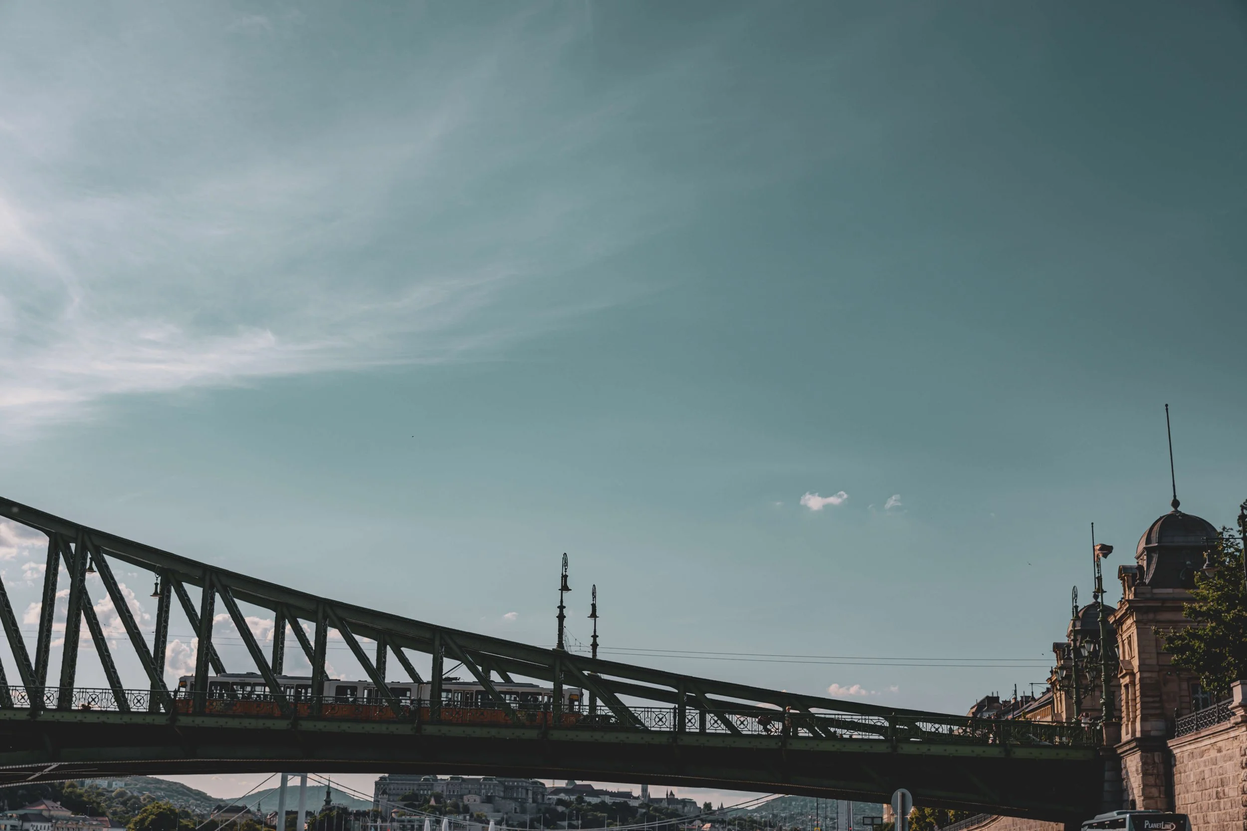 Image of a cityscape with a bridge, ornate buildings, and lamp posts against a blue sky with some clouds.