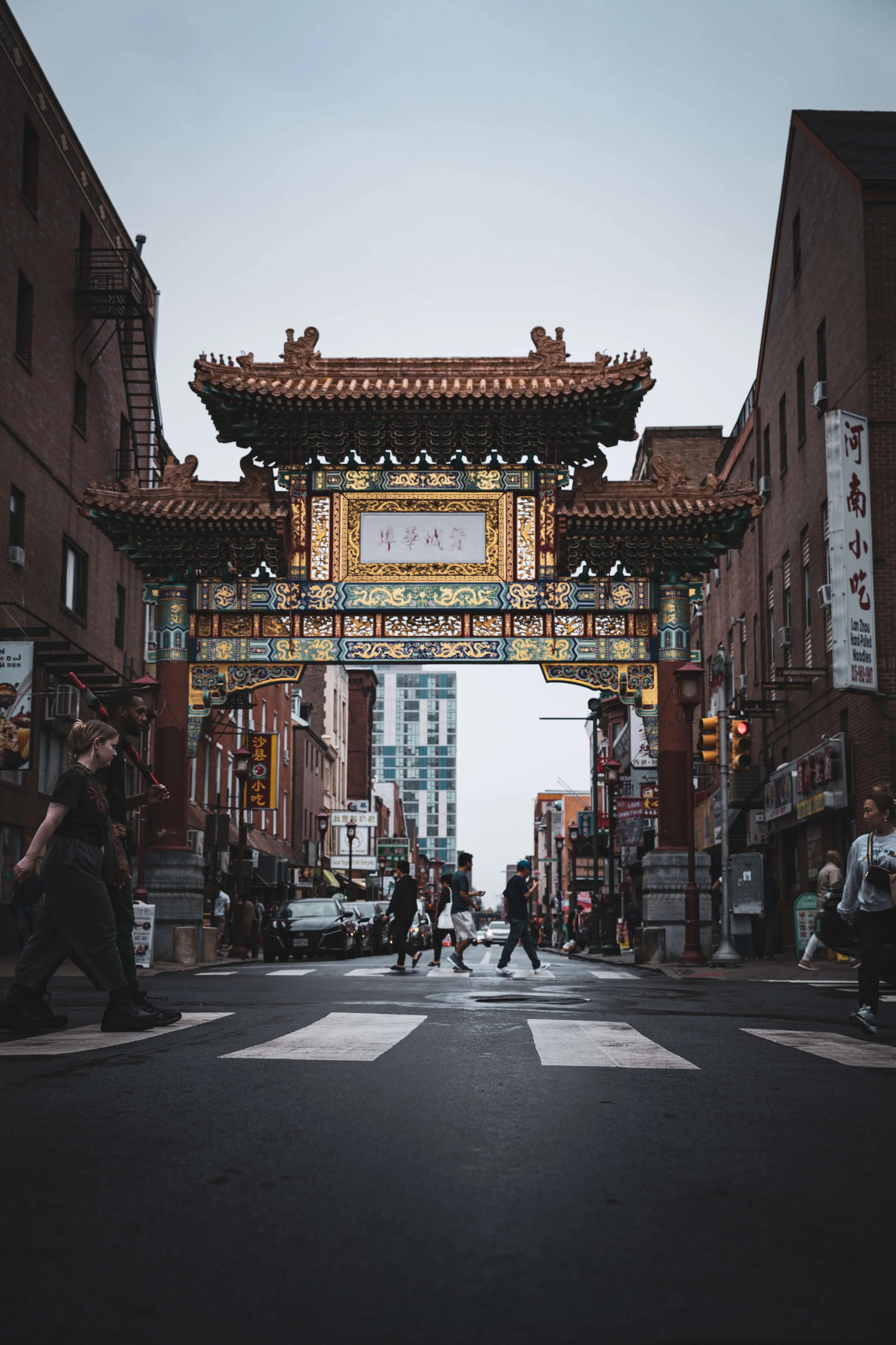 A street scene with a traditional Chinese archway, pedestrians crossing the road, and buildings on either side.