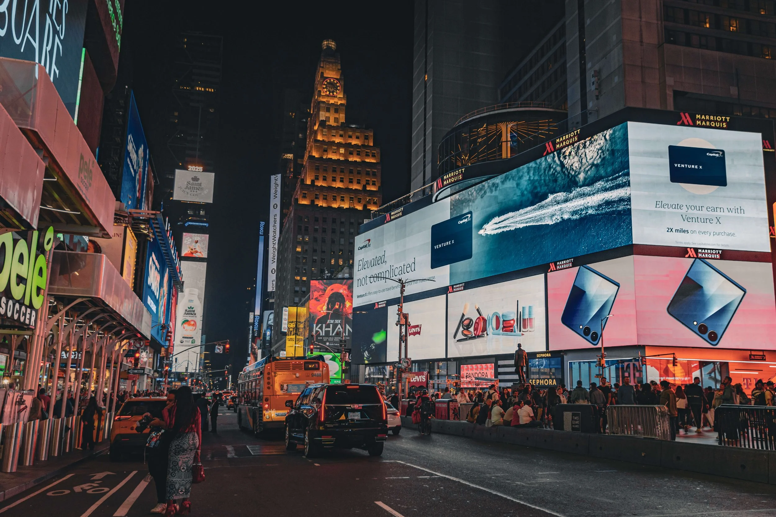 Bright digital billboards and advertisements illuminated in Times Square at night, with crowded pedestrians and vehicles.