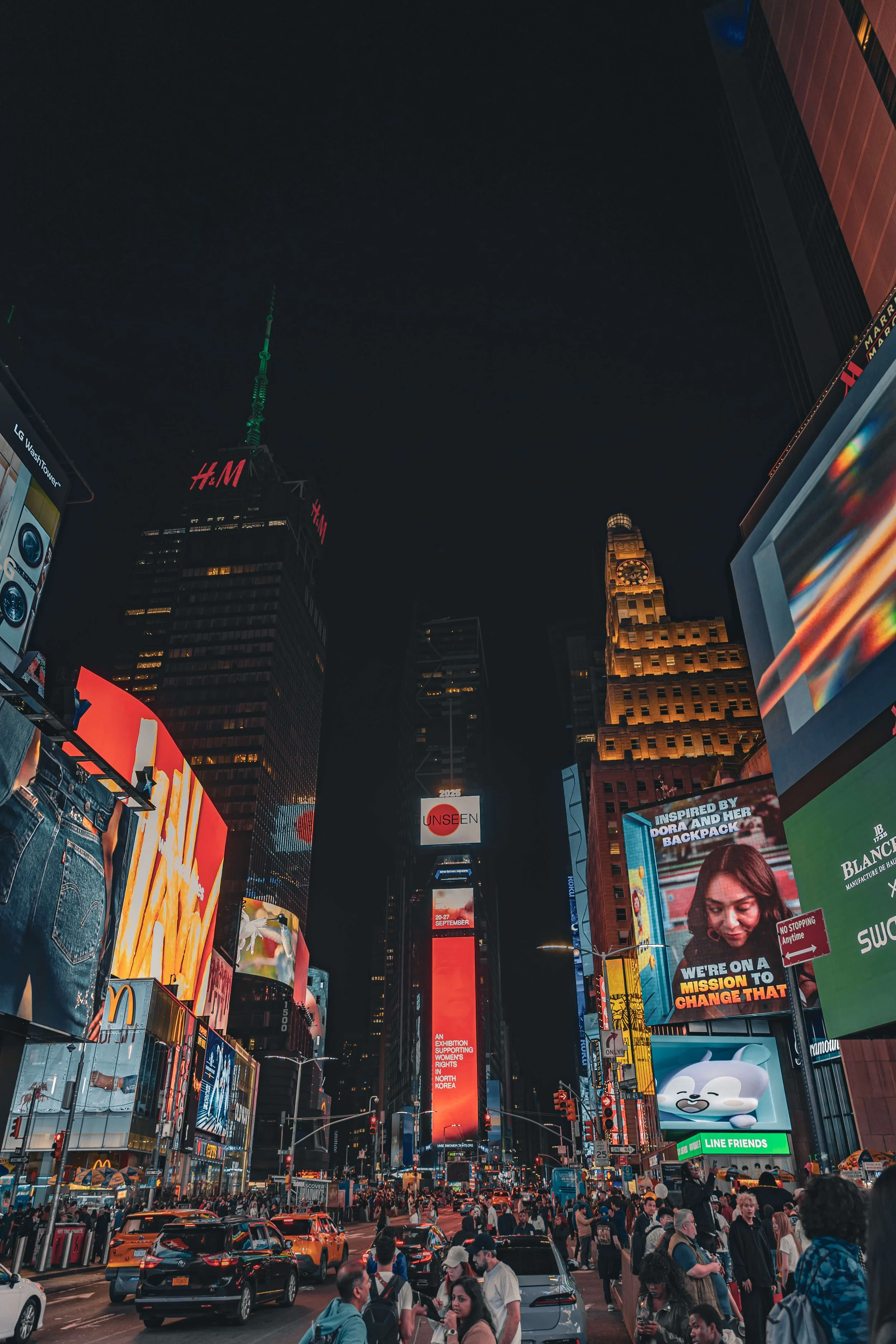 A lively night scene in Times Square, New York City, with crowds of people on the street, numerous brightly lit billboards, taxis, and tall buildings with illuminated signs.