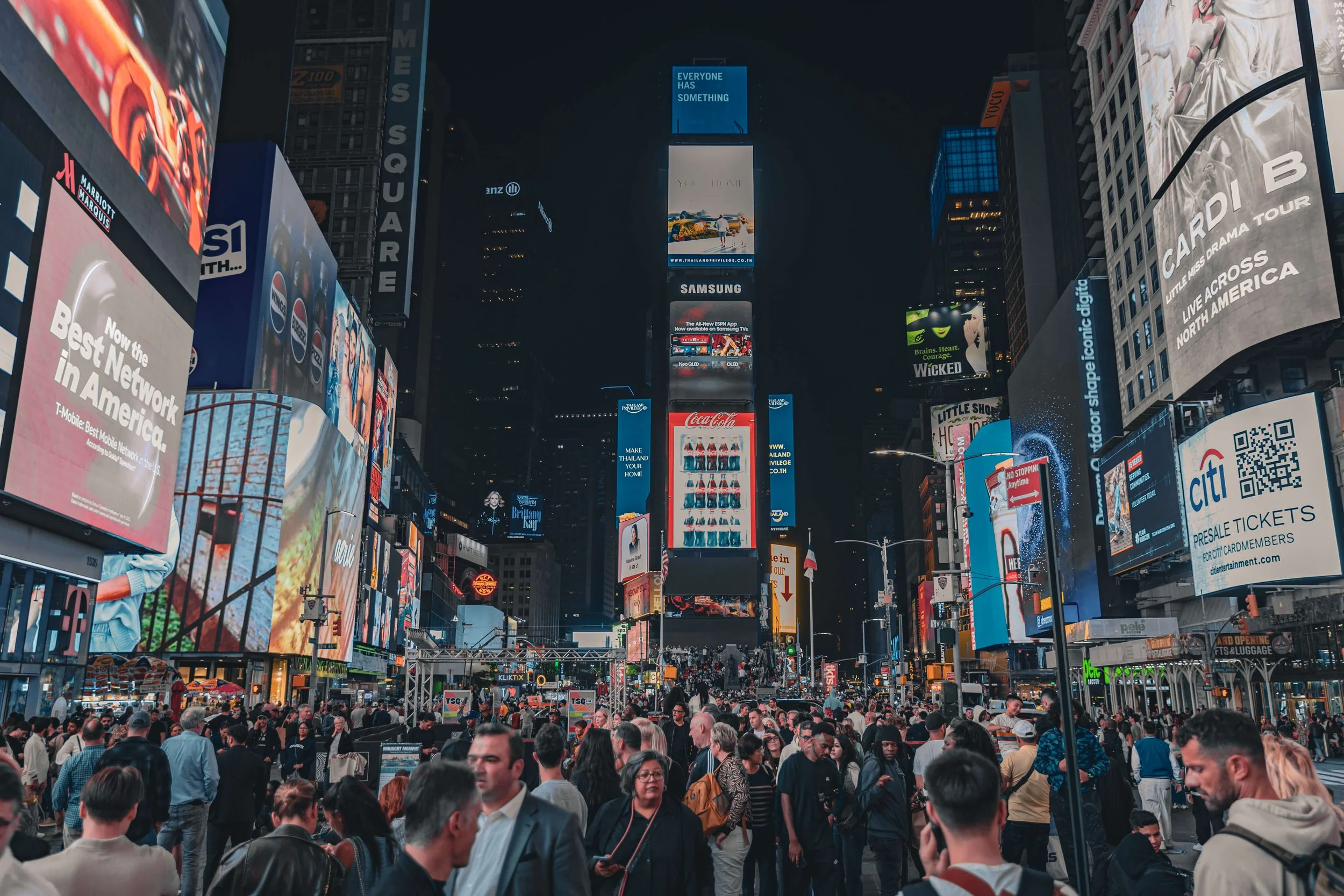 Crowded Times Square at night with bright electronic billboards and advertisements.