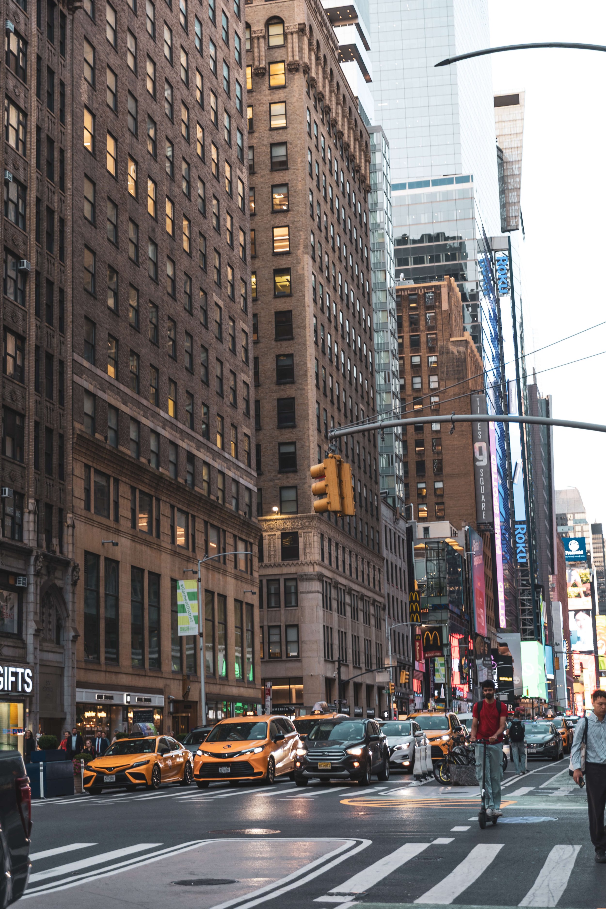 Busy city intersection with tall buildings, yellow taxis, and pedestrians, in Times Square area.