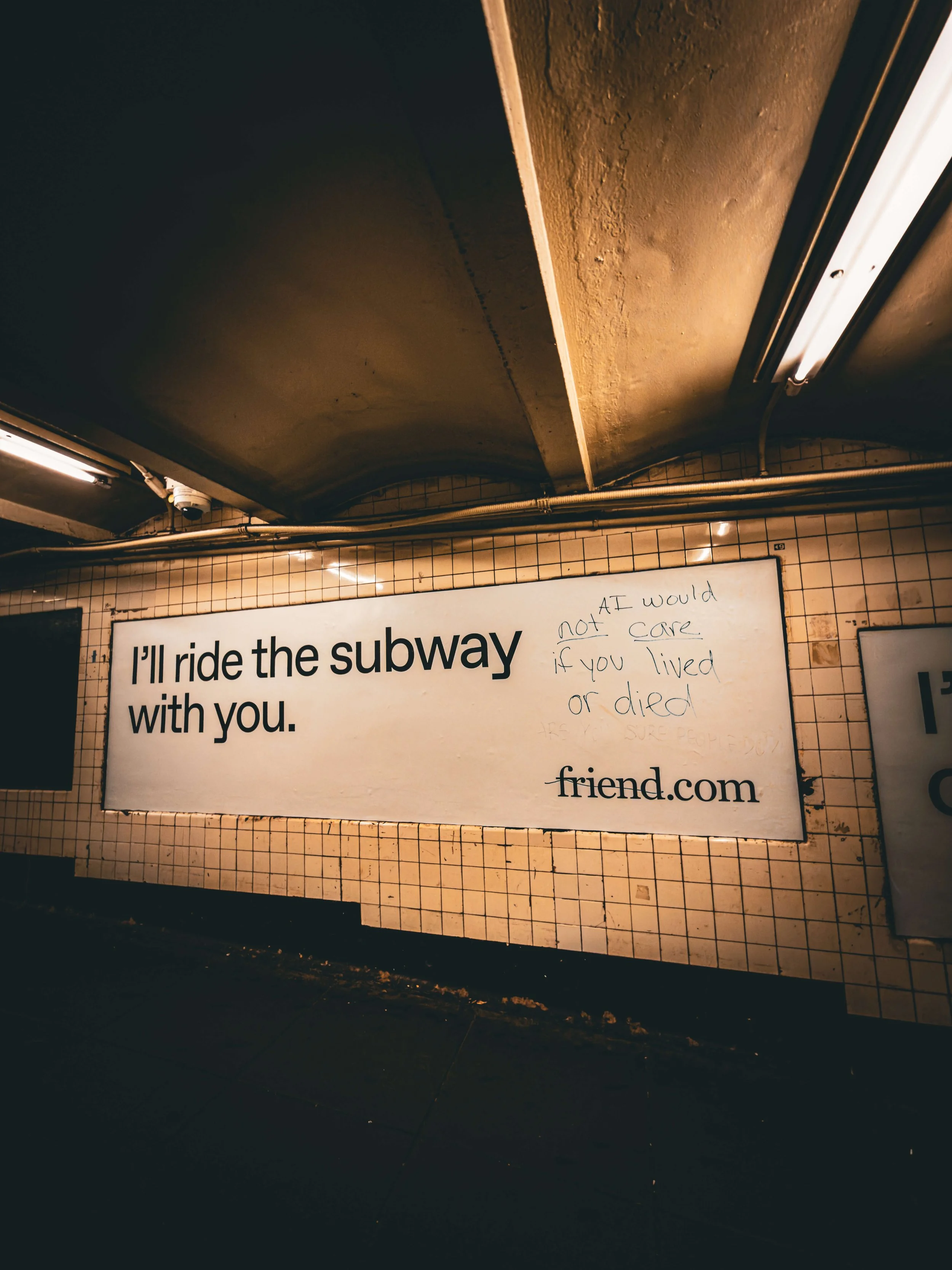 A large white advertisement sign in a subway station that reads 'I'll ride the subway with you.' The sign has handwritten notes on it that say 'AT would not care if you lived or died.' The background includes tiled walls and fluorescent lighting.