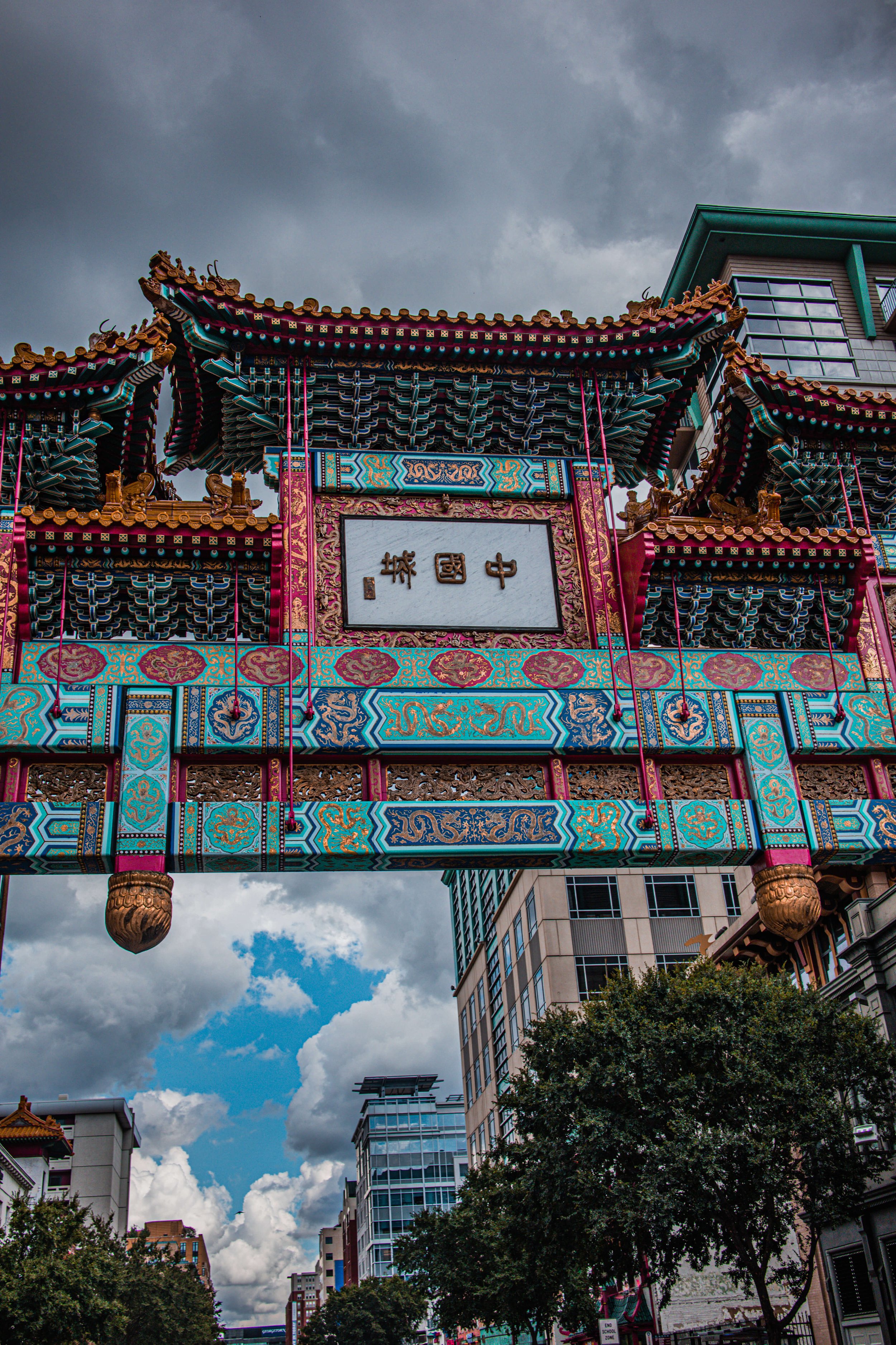 Colorful Chinese archway in an urban setting with modern buildings and a partly cloudy sky.
