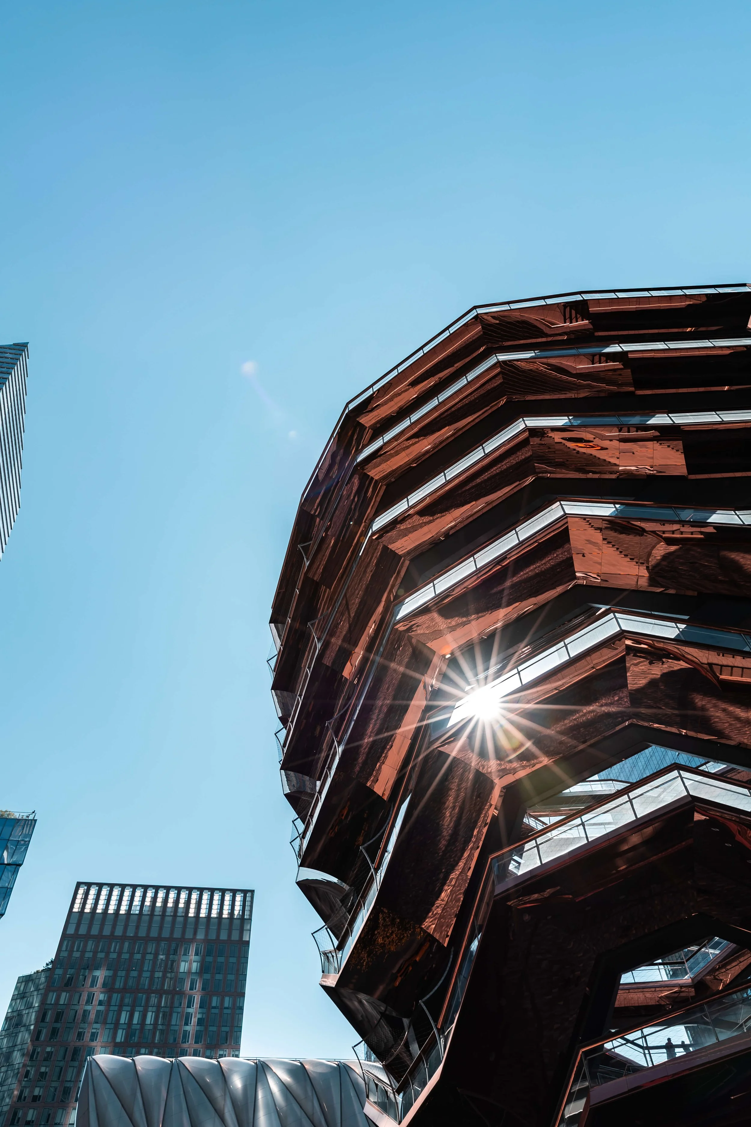 Modern glass building with reflective copper-colored exterior, sunlight shining through, against a clear blue sky.