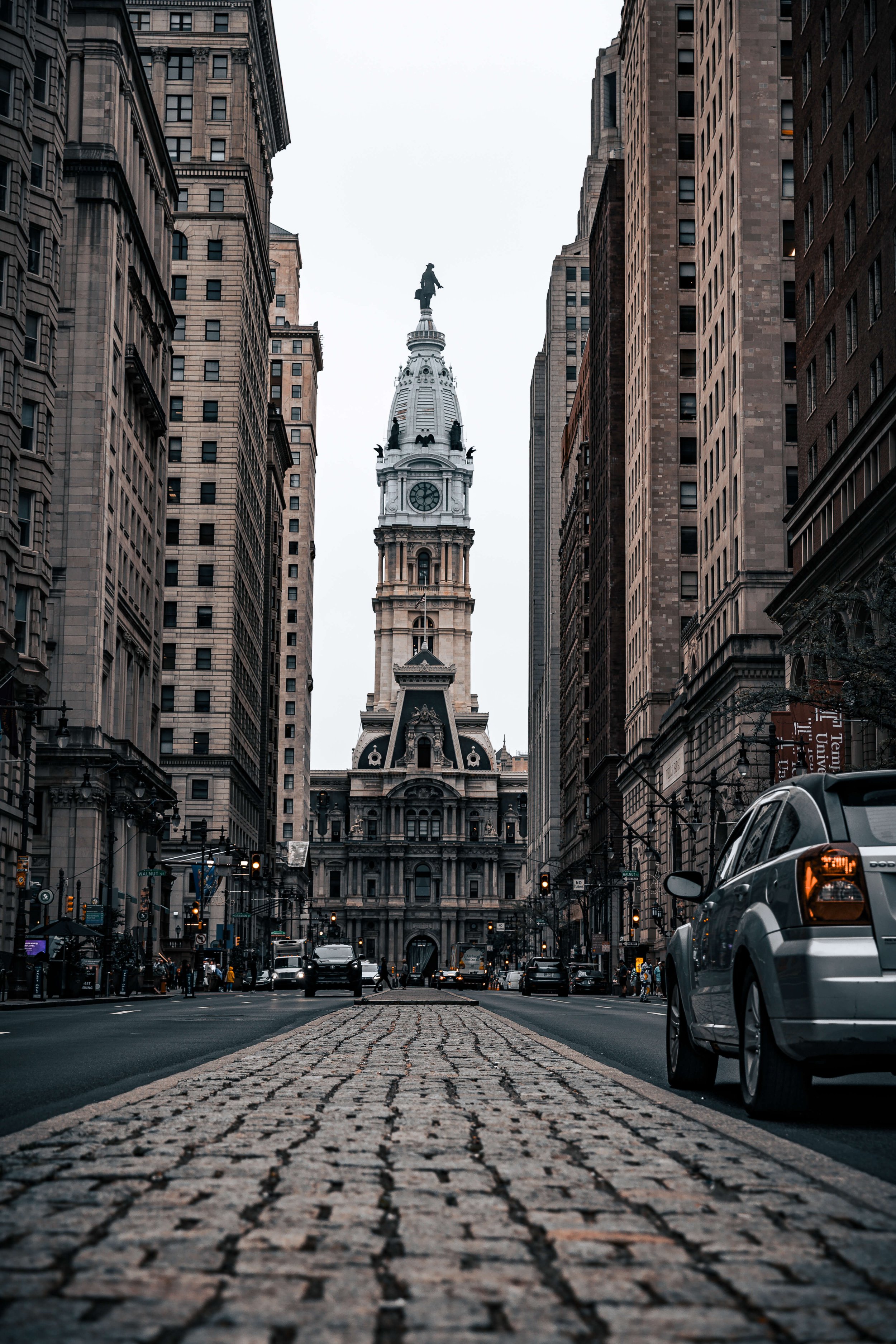 Street view of Philadelphia City Hall, with tall buildings on both sides and a cobblestone road in the foreground.