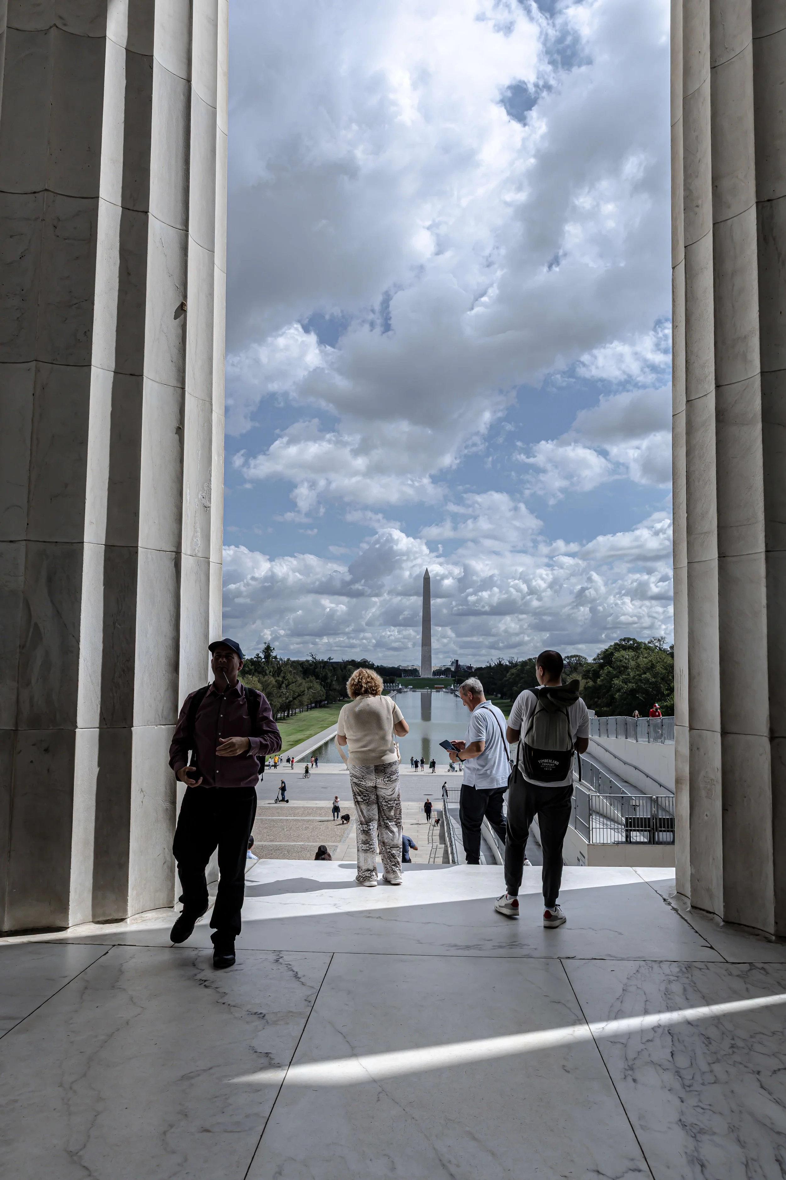 View of the Washington Monument through the arch of the Lincoln Memorial with several visitors standing and walking.