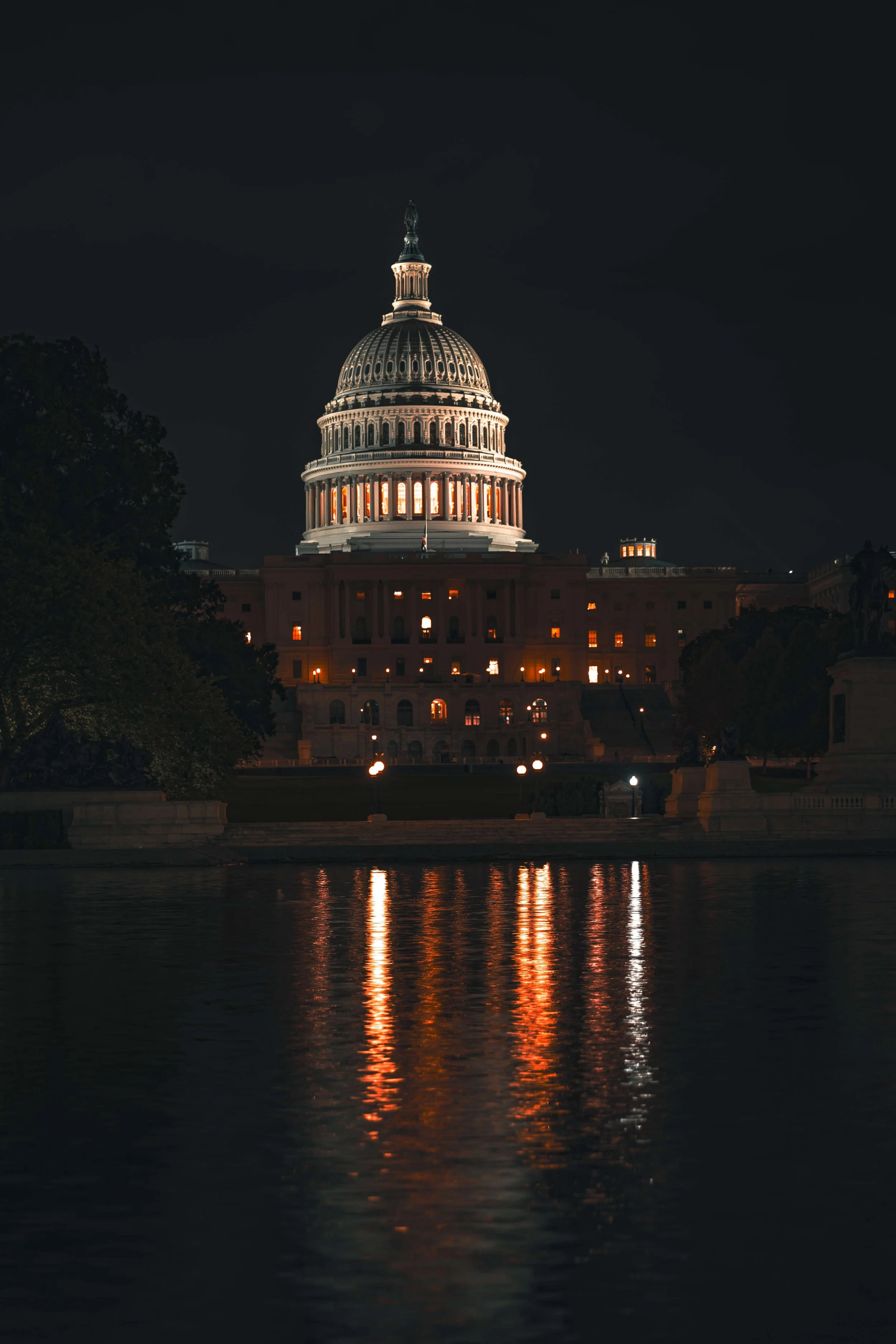 Night view of the illuminated United States Capitol building reflected on the water.