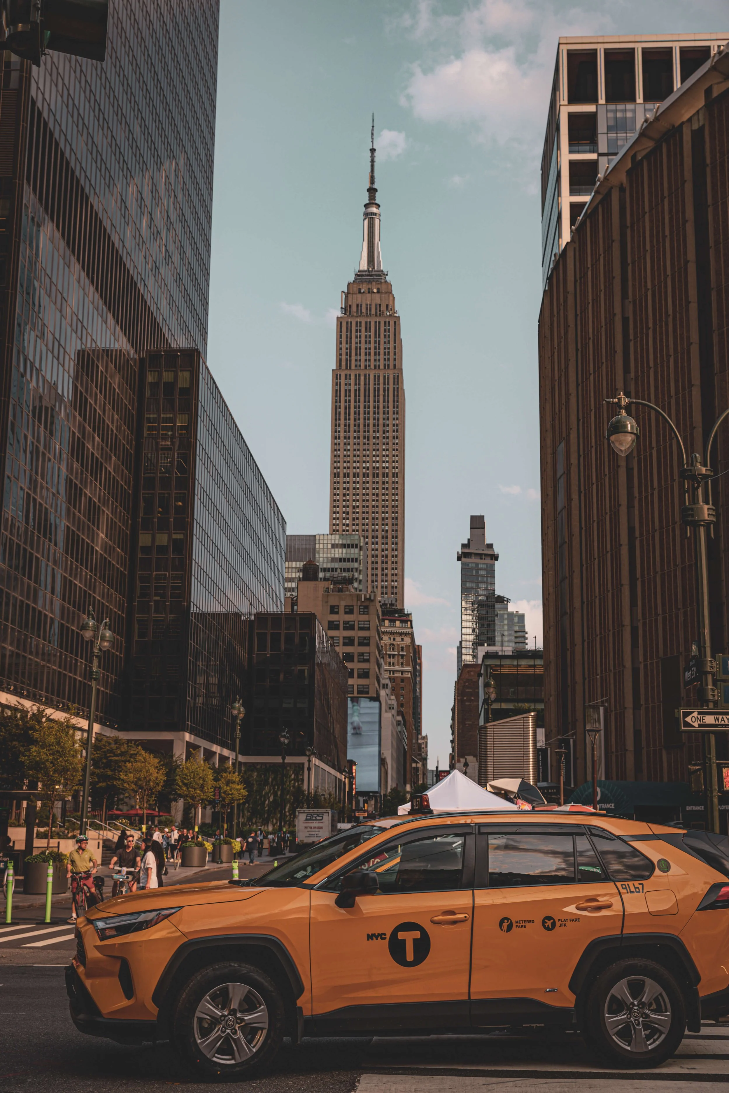 A yellow NYC taxi cab on a city street with the Empire State Building in the background.