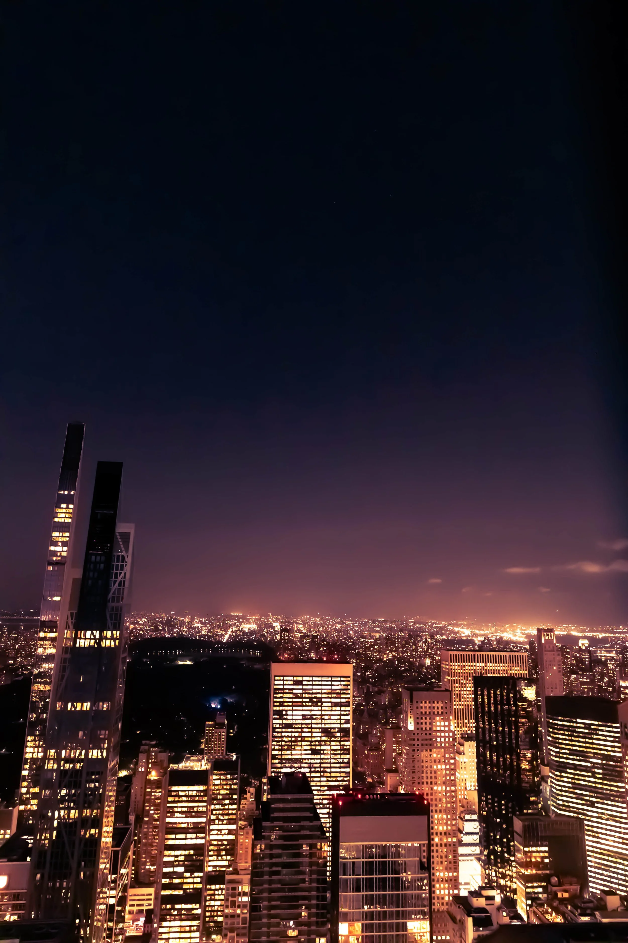Night view of a city skyline with tall buildings illuminated, sky dark with no visible stars or moon.