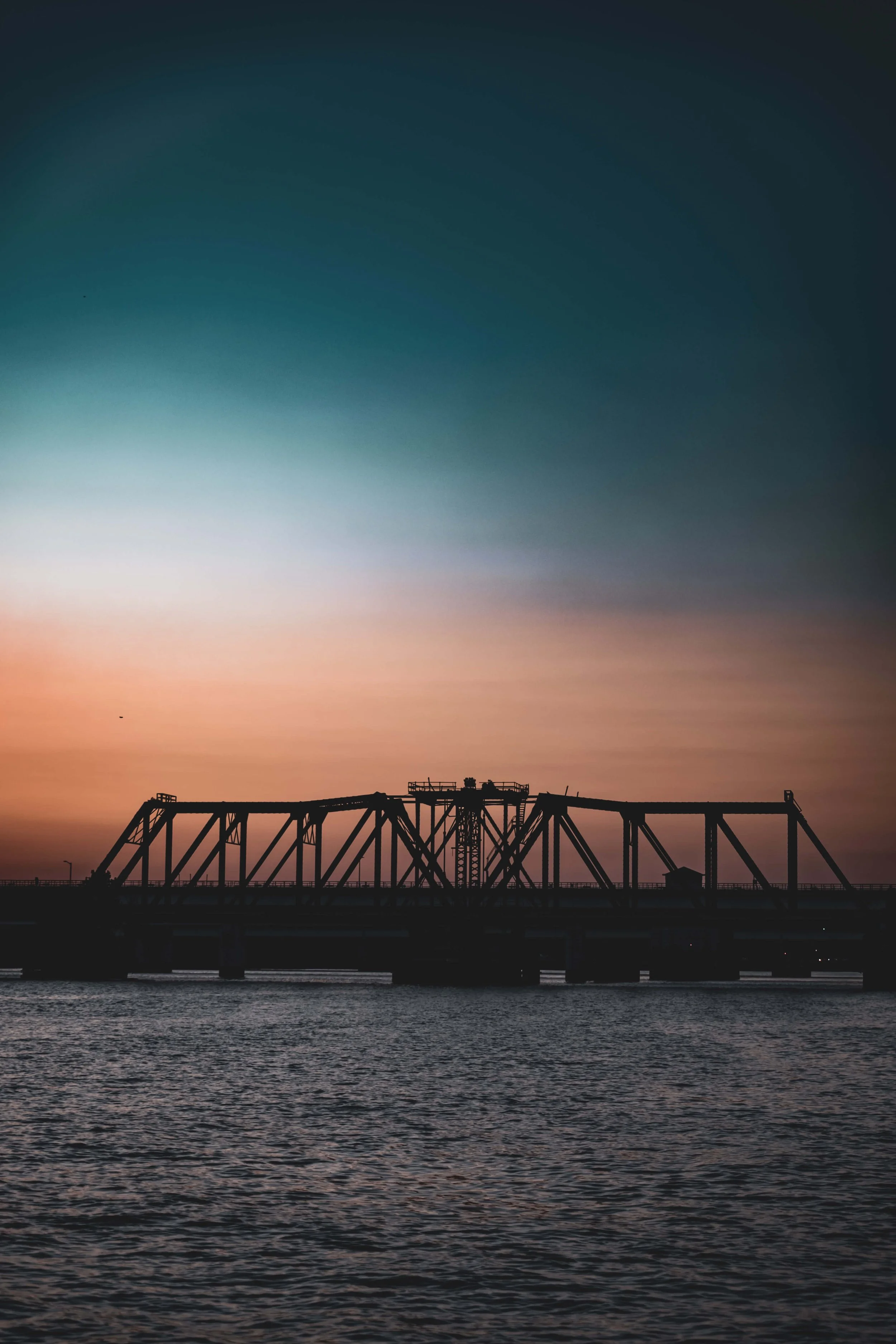 Silhouette of a bridge over water during sunset with a colorful sky.