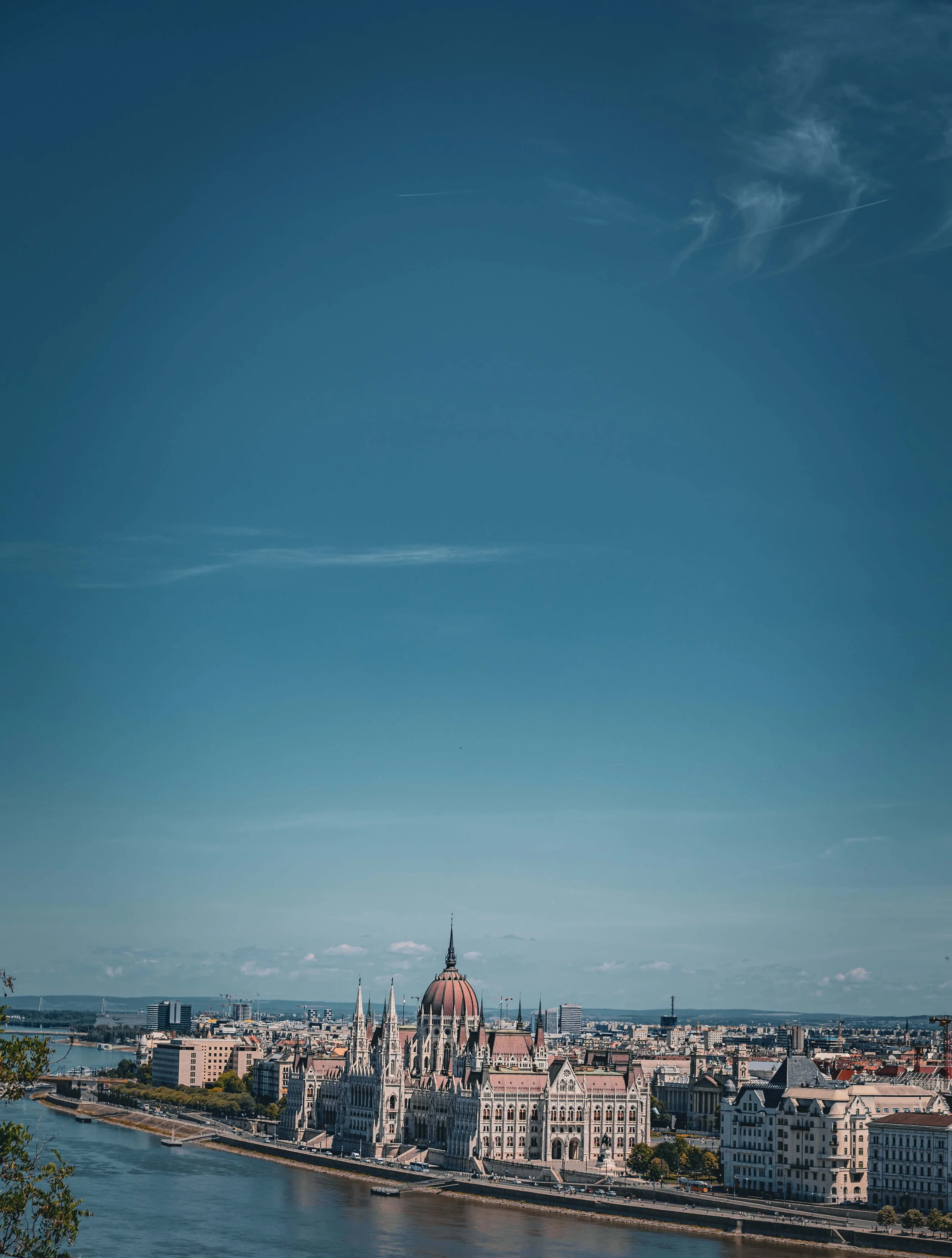 A panoramic view of Budapest featuring the Hungarian Parliament building along the river, with a clear sky above and a distant skyline.