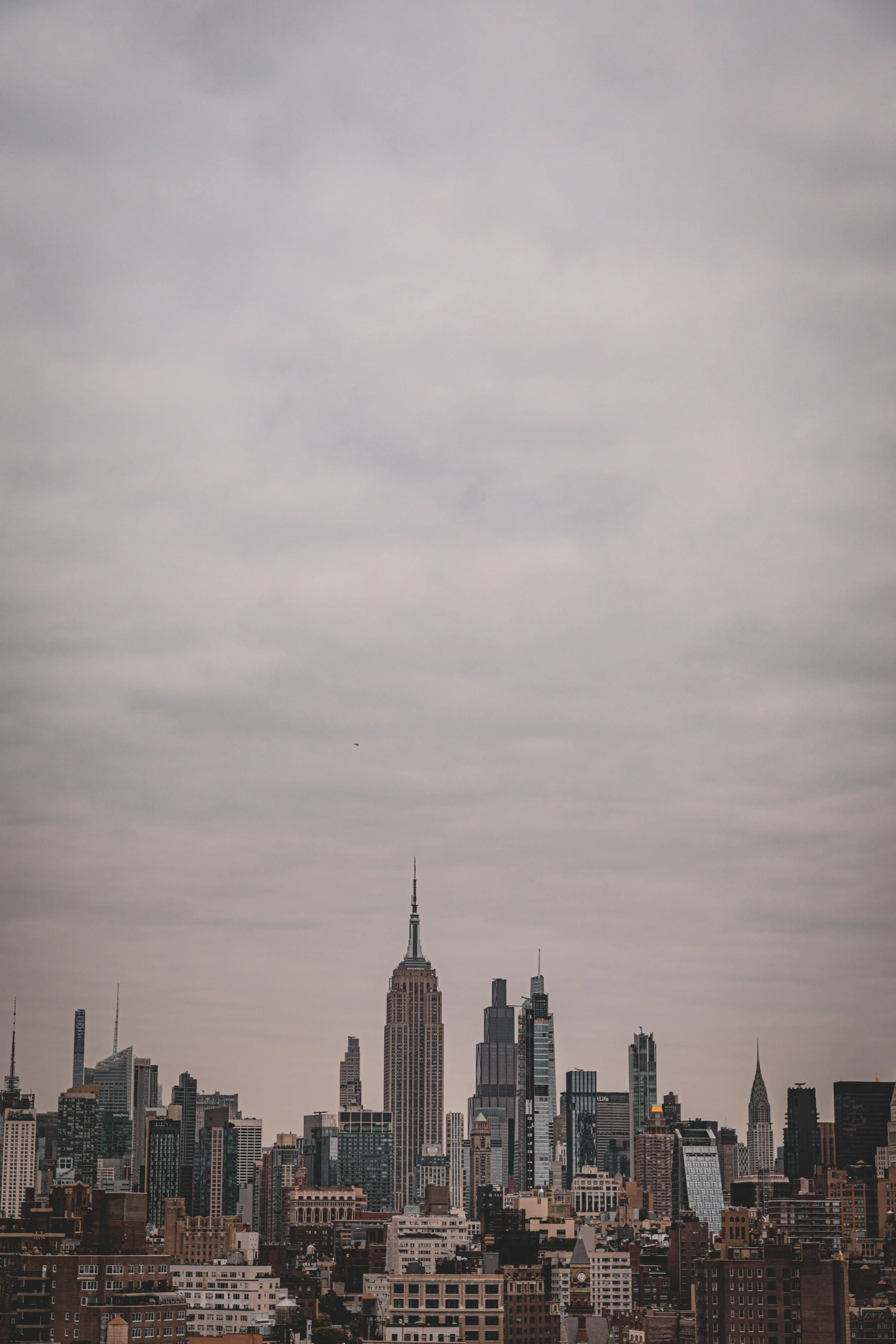City skyline featuring the Empire State Building among other skyscrapers under cloudy sky.
