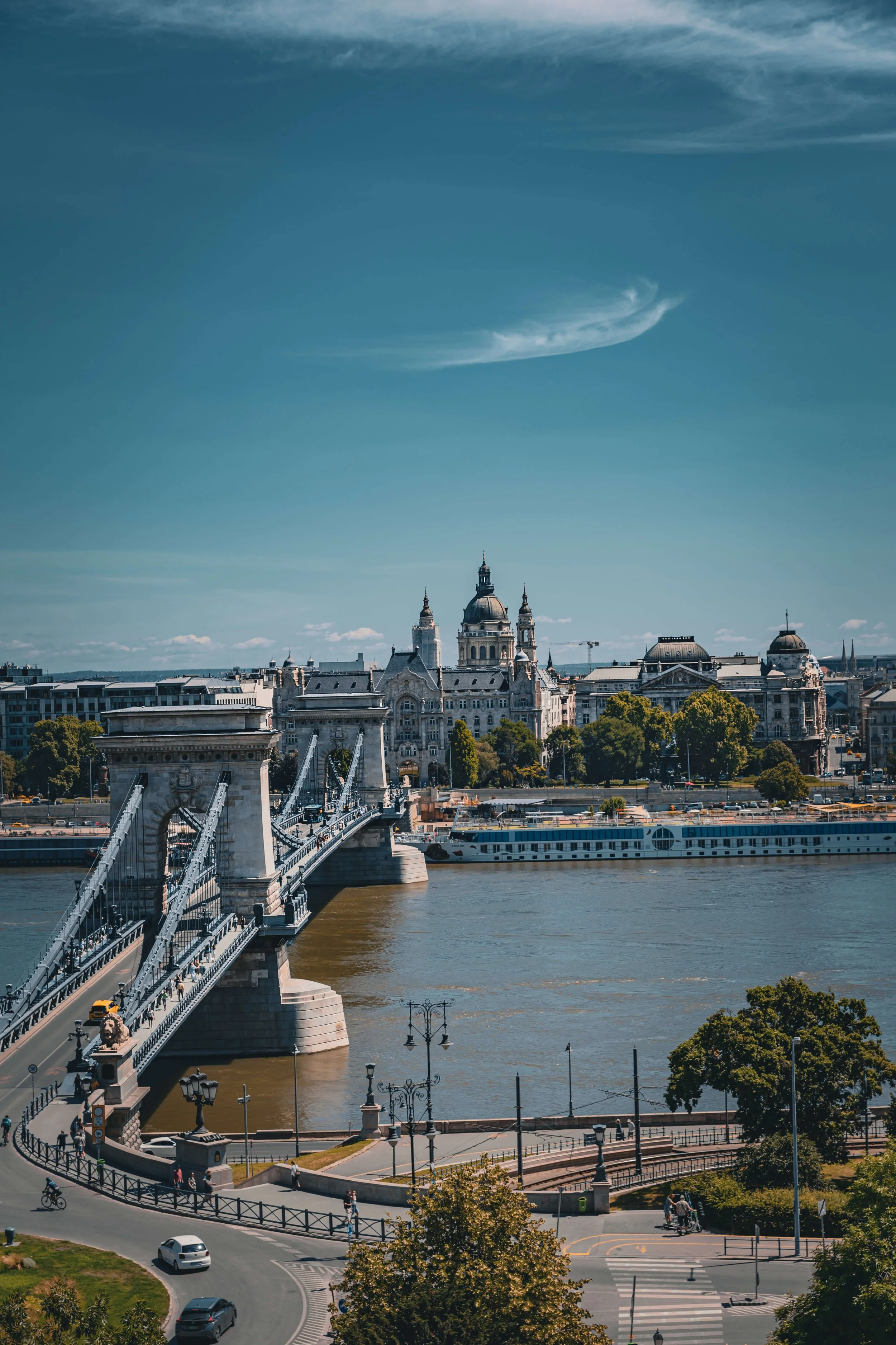 View of a city skyline with historic buildings, a bridge crossing a river, and a blue sky with clouds.