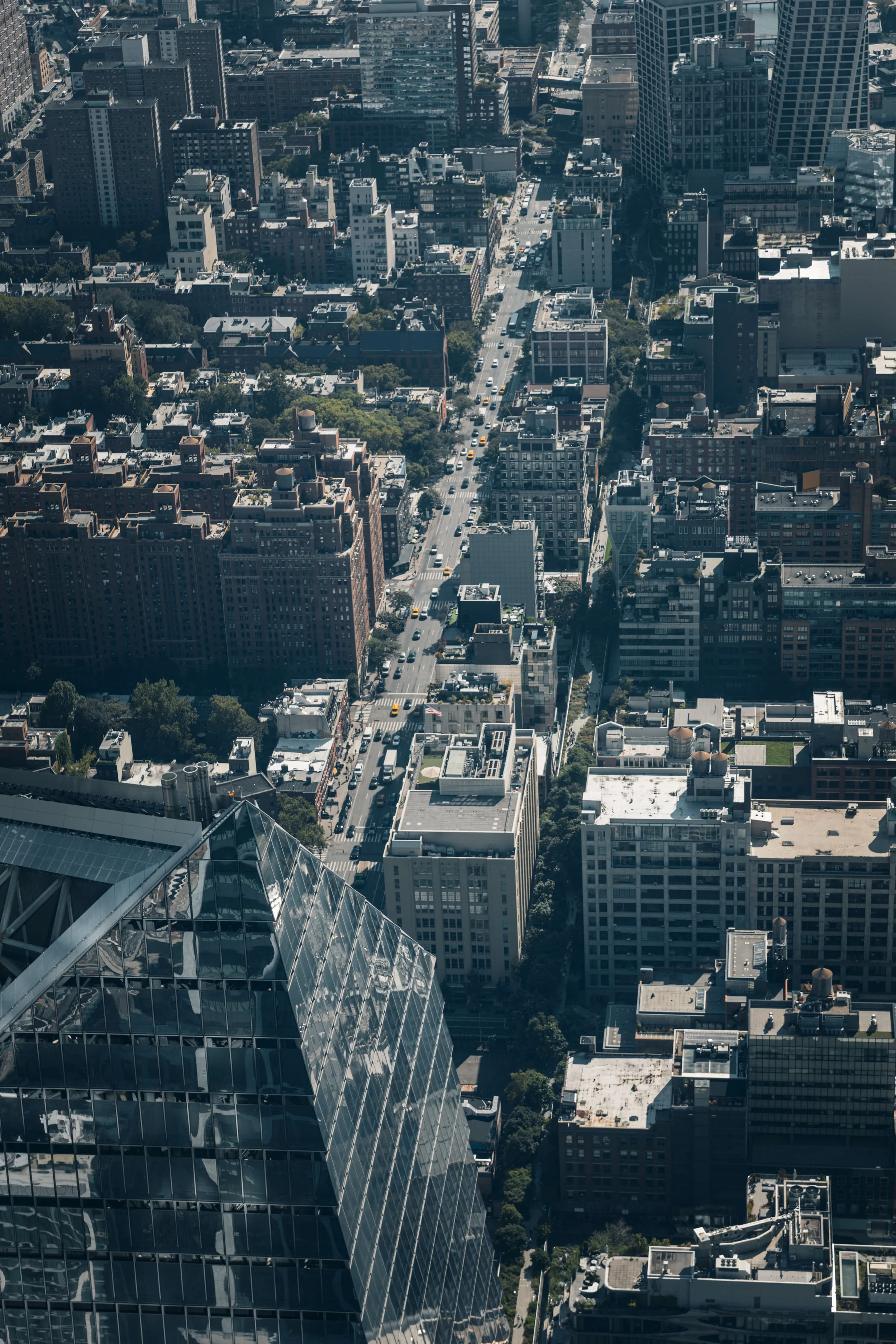 An aerial view of a city with tall buildings, streets filled with cars, and a glass skyscraper in the foreground.