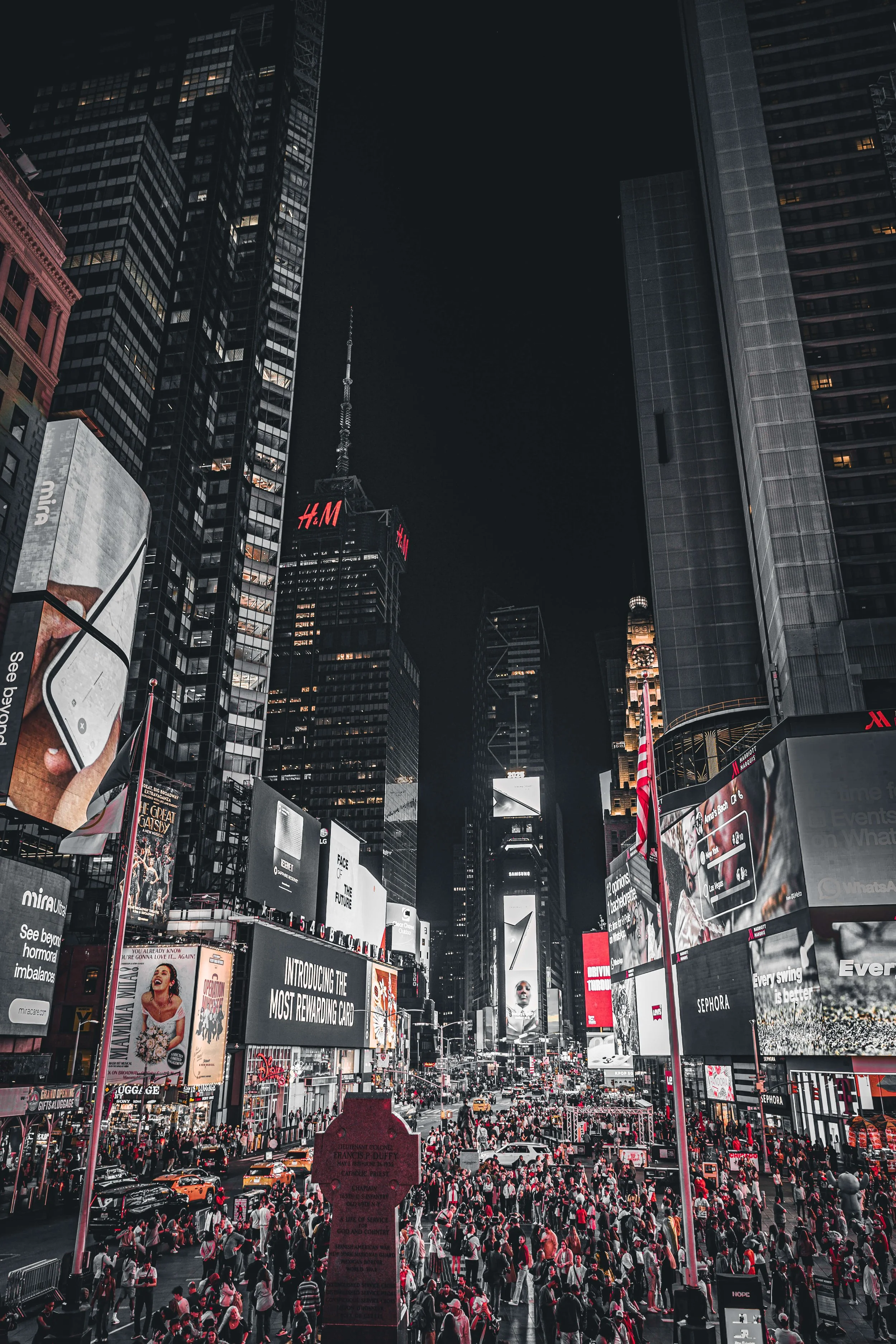 Nighttime scene in Times Square with large digital billboards, illuminated advertisements, and a crowd of people.