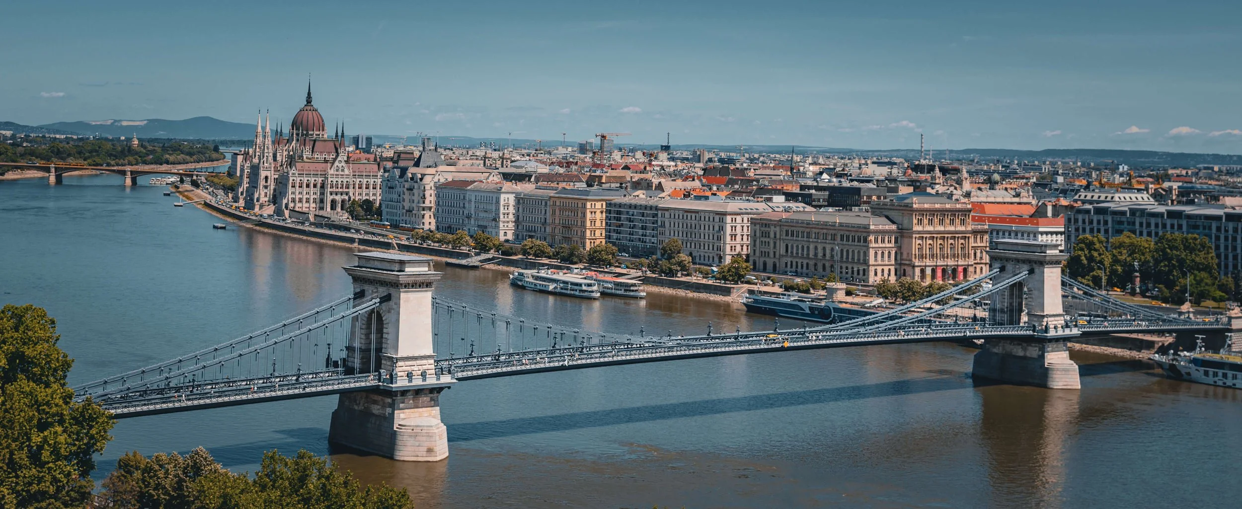 Aerial view of Budapest, Hungary, showing the Chain Bridge crossing the Danube River with the Hungarian Parliament Building in the background.