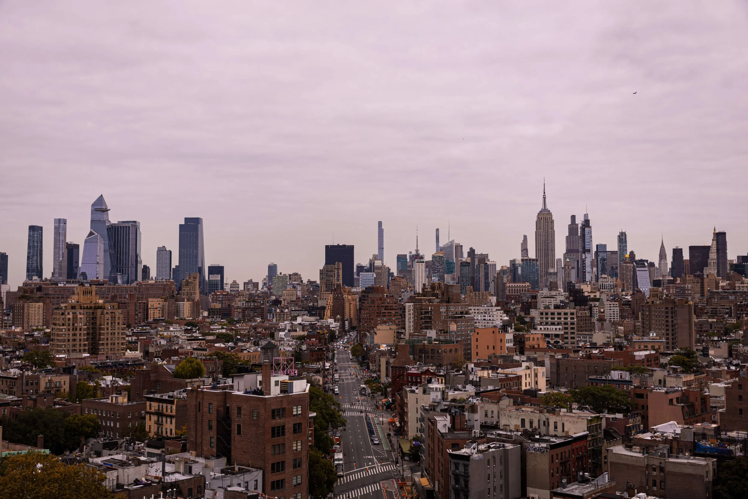 City skyline of New York City with tall skyscrapers and Empire State Building under cloudy sky.