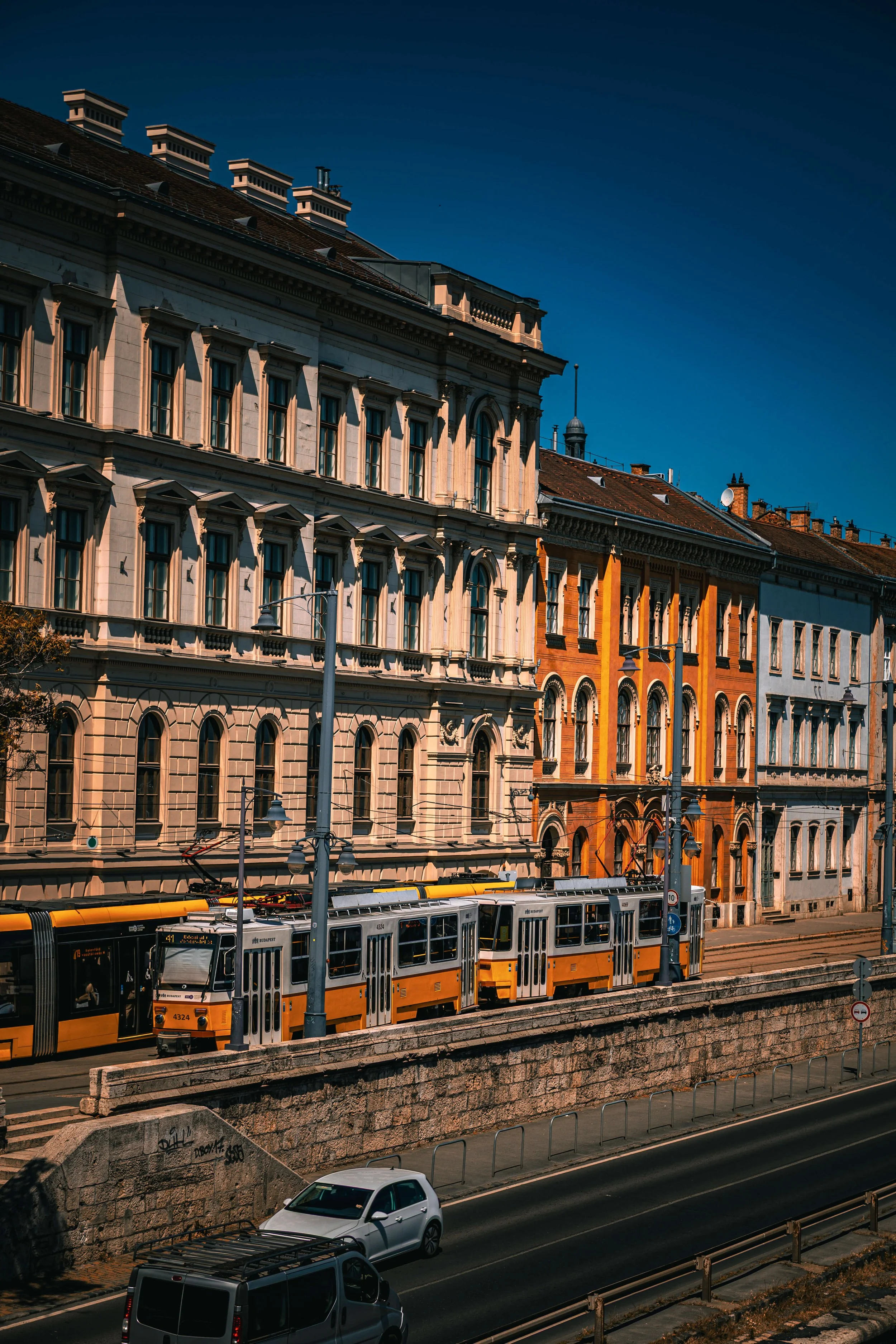 City street with historic buildings, tram, and cars on the road, under a dark blue sky.