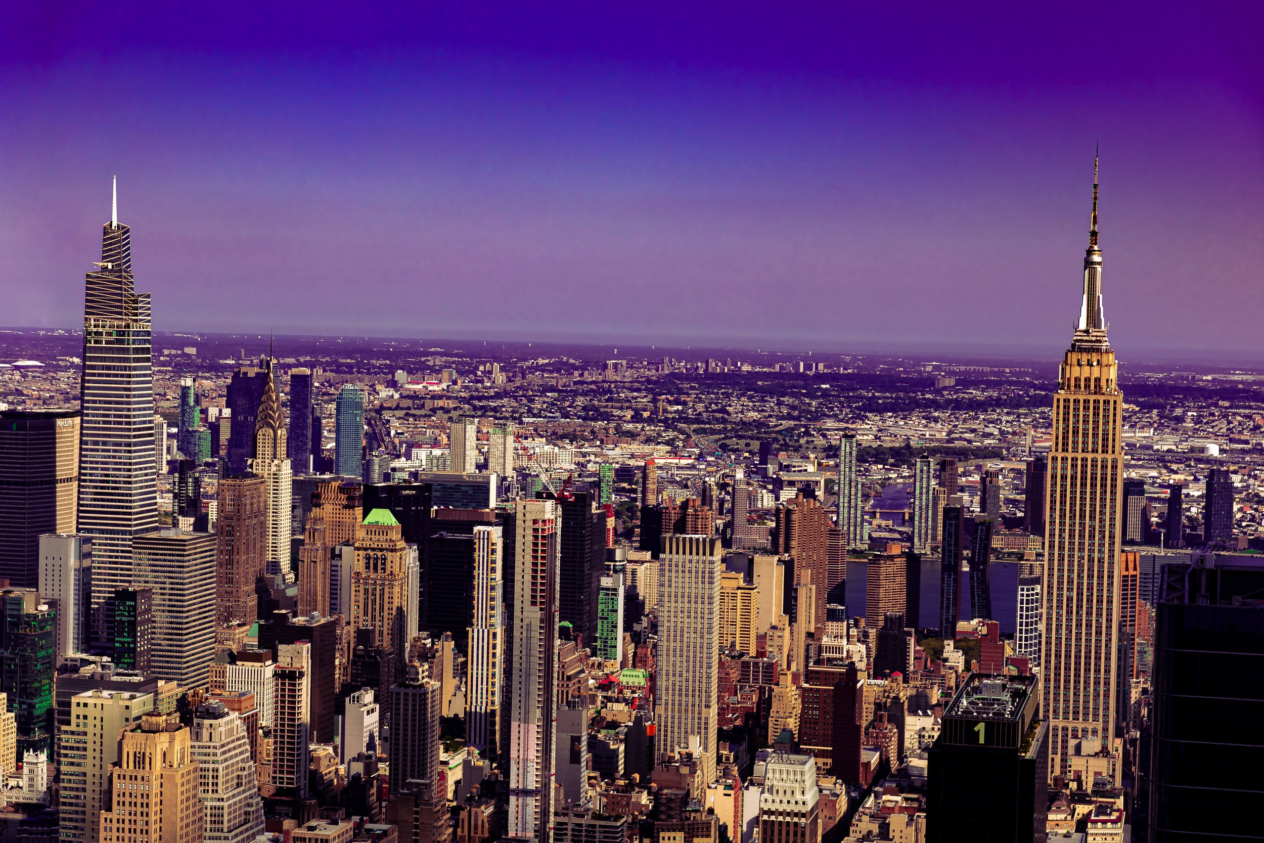 Aerial view of the New York City skyline featuring the Empire State Building and other skyscrapers under a purple sky.