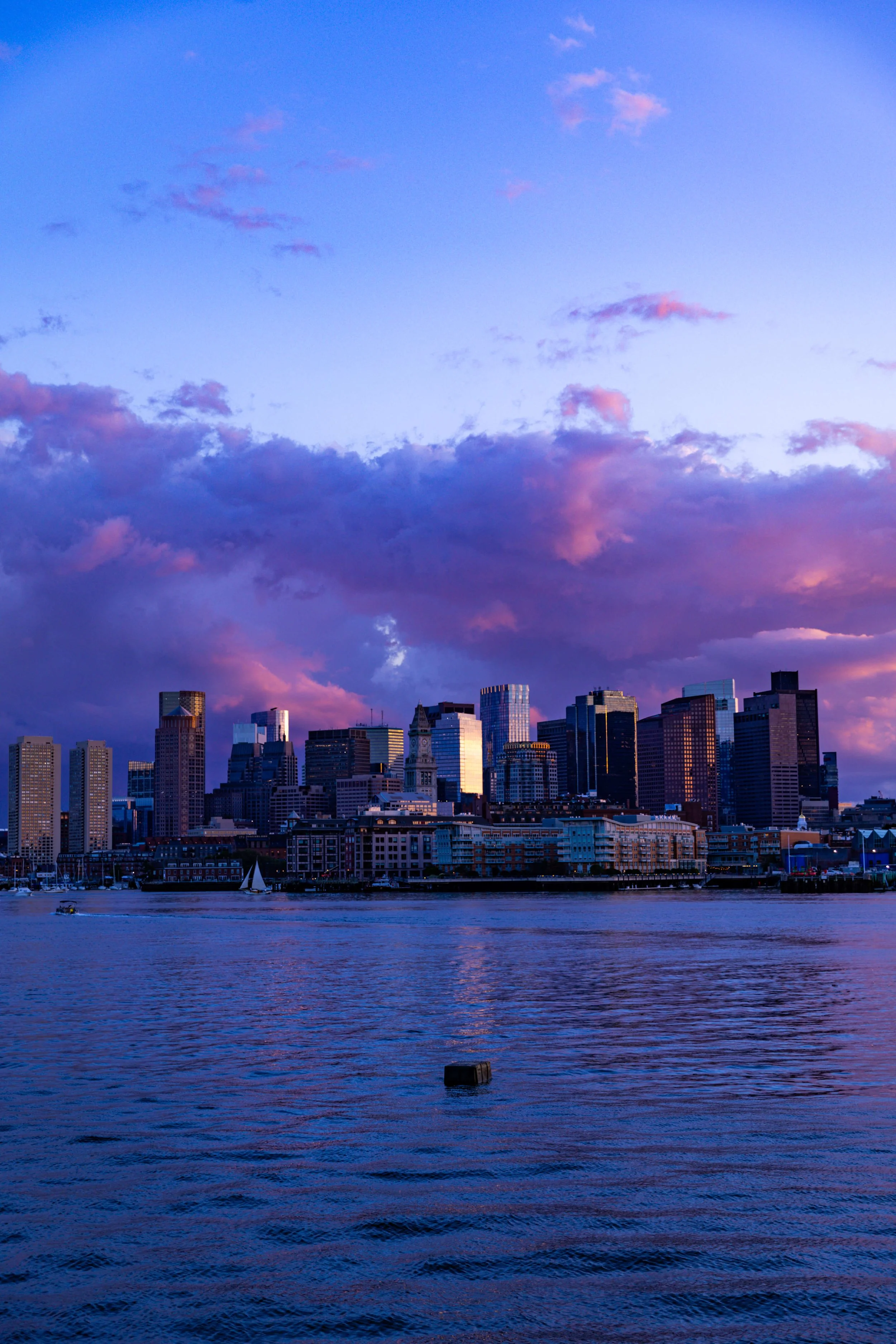 View of a city skyline at sunset with purple clouds over the water.