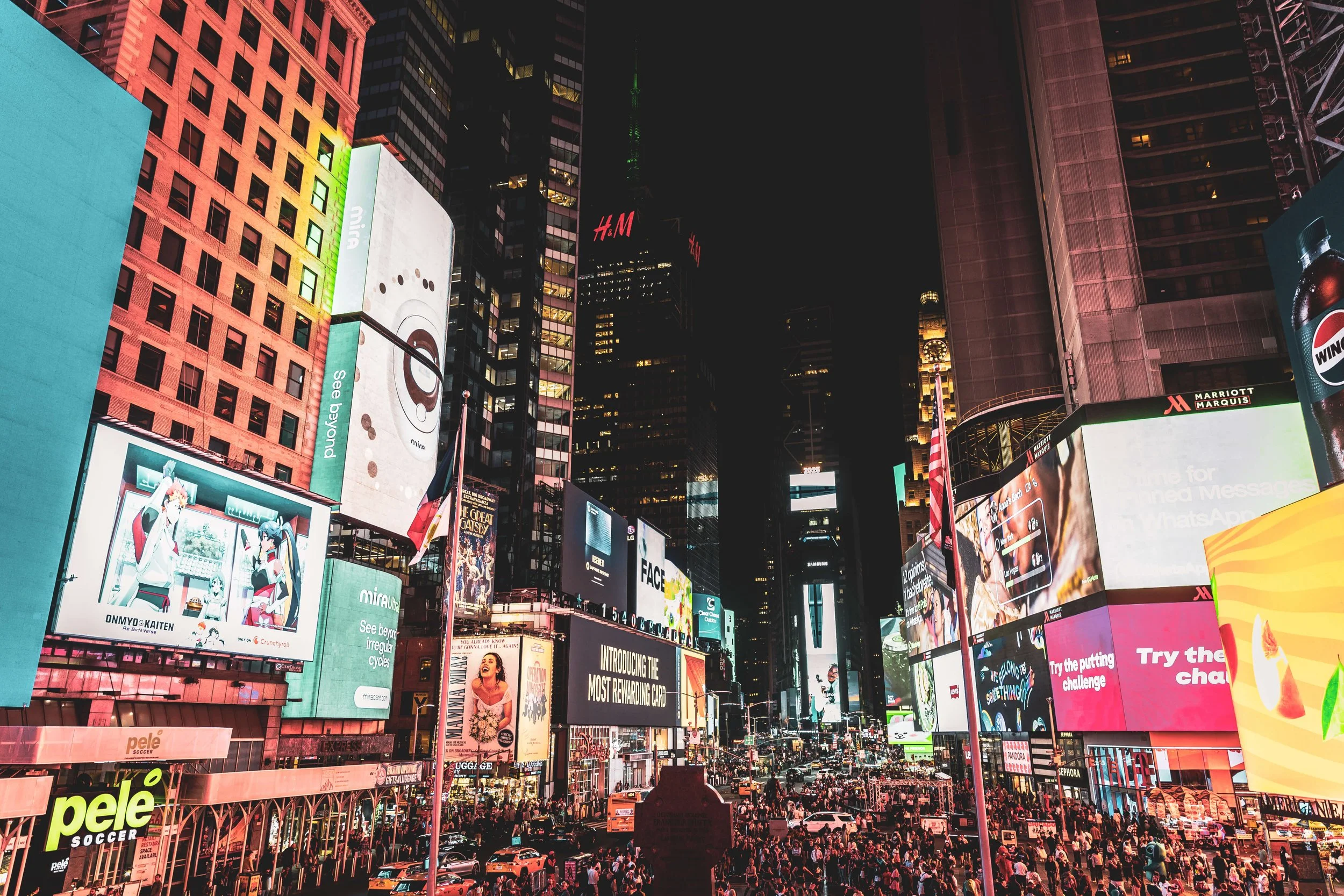 Busy Times Square at night with bright digital billboards and crowds of people.