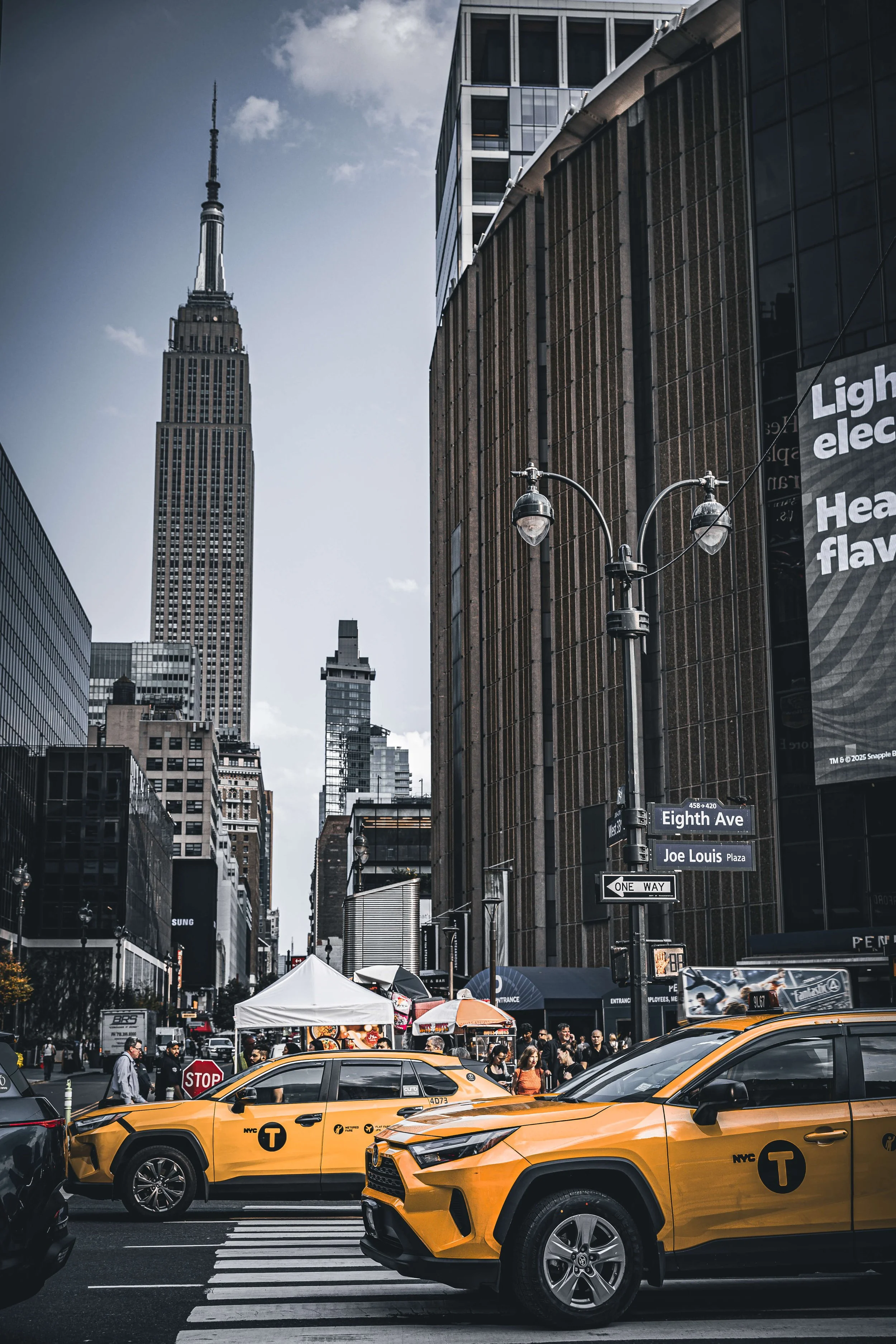 City street scene in New York City with taxis, pedestrians, tall buildings, and the Empire State Building in the background.