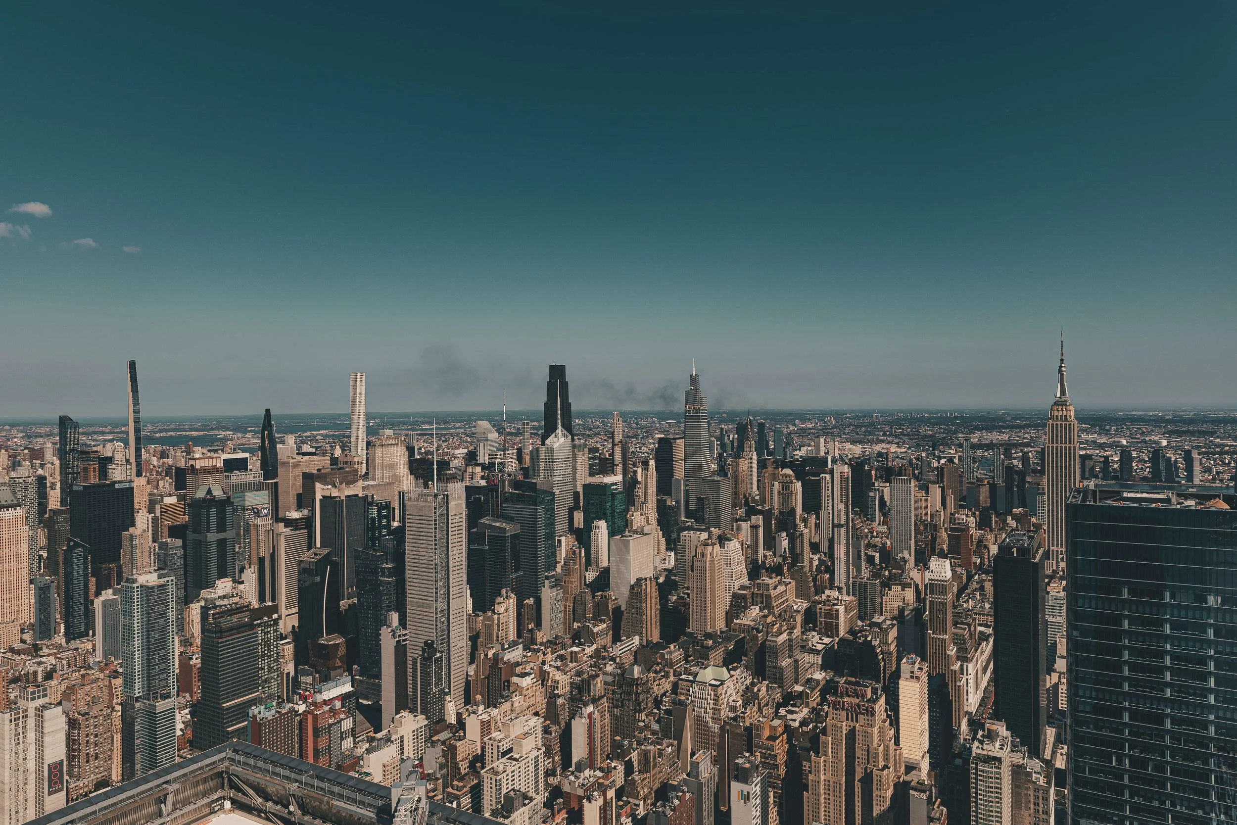 Aerial view of the New York City skyline with numerous skyscrapers including the Empire State Building and other famous buildings, under a clear blue sky.