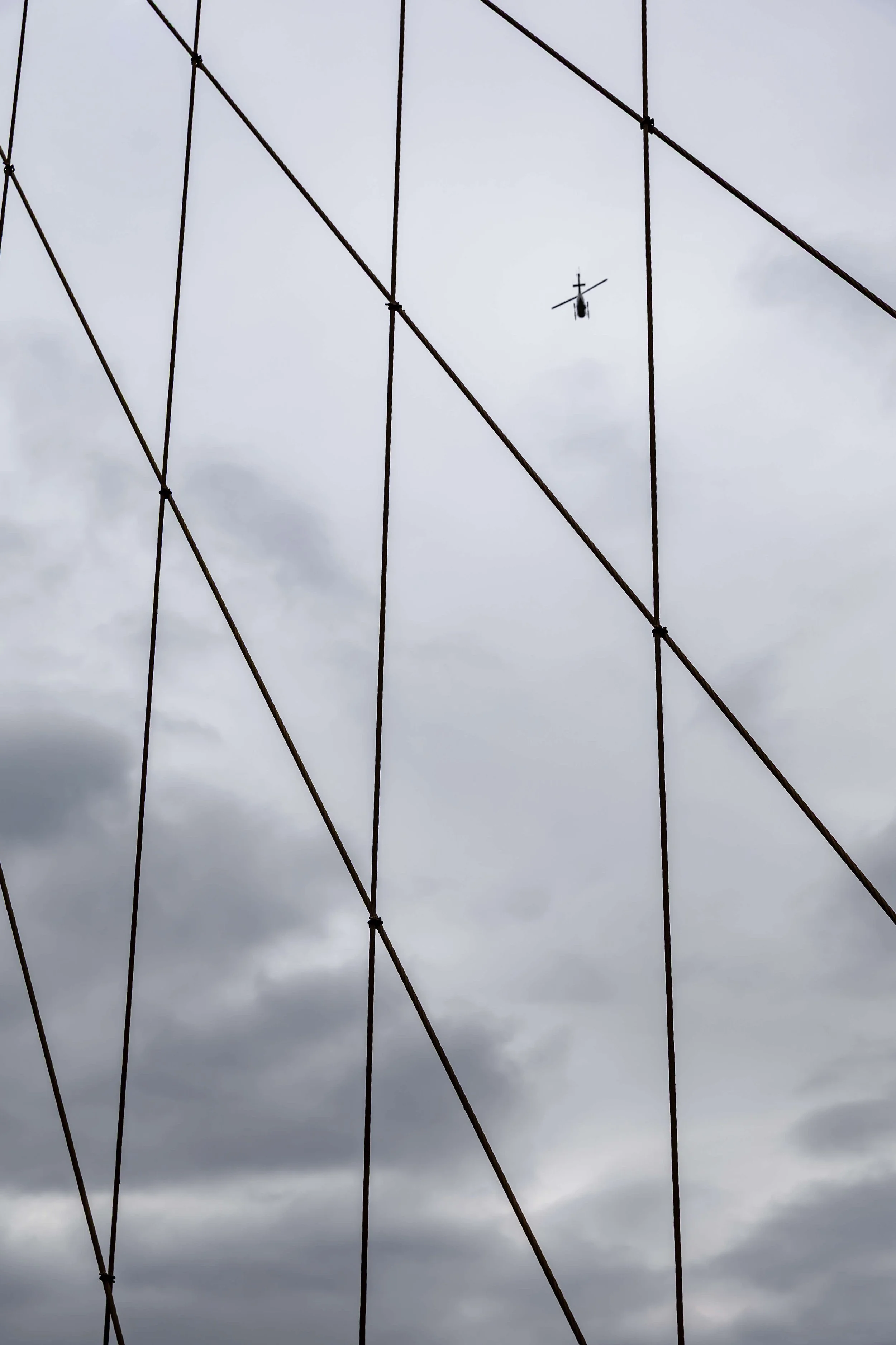 A helicopter flying in a cloudy sky seen through a wireframe structure.