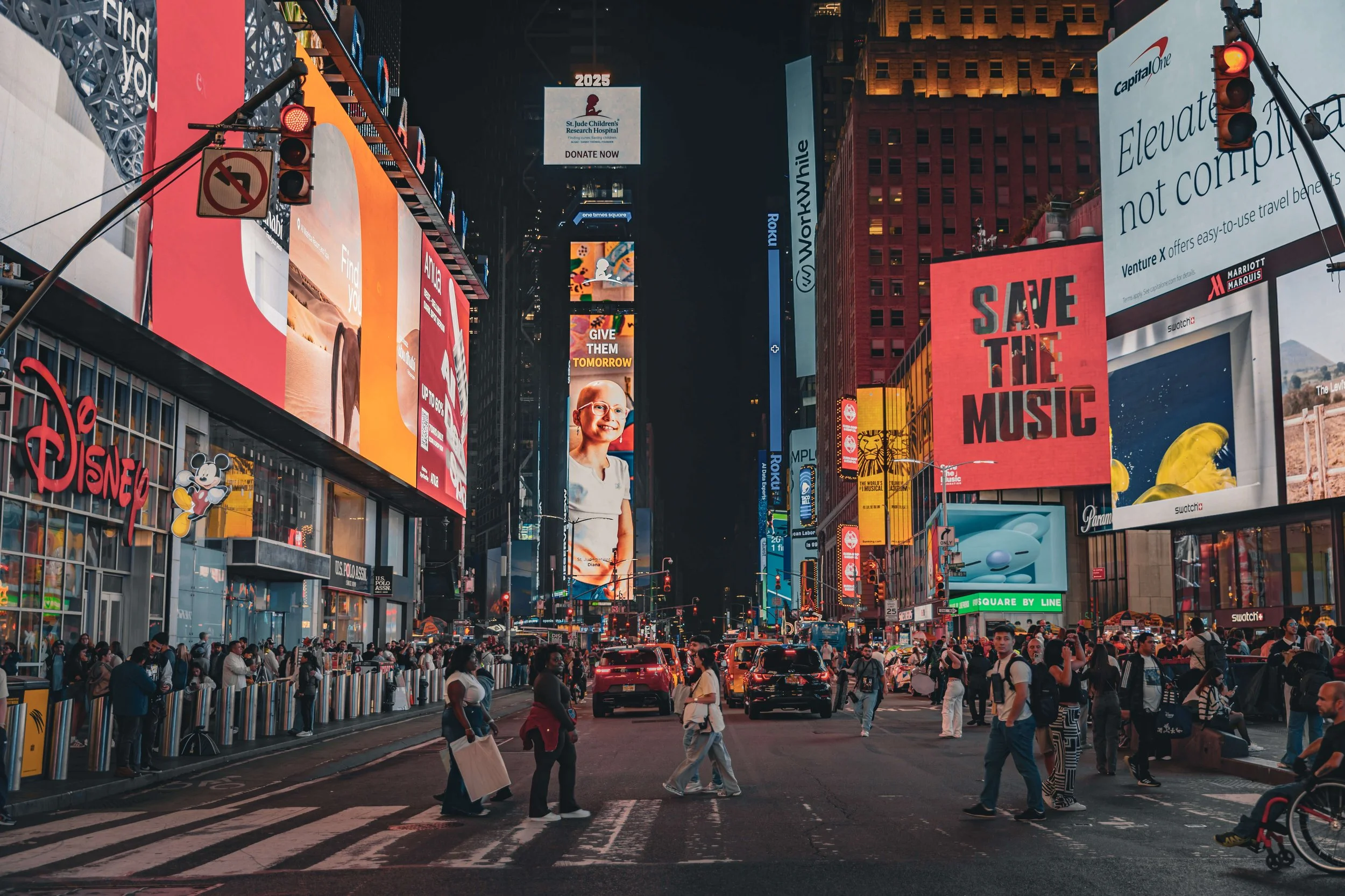 Nighttime scene in Times Square, New York City with bright digital billboards, advertisements, and crowds crossing the street.