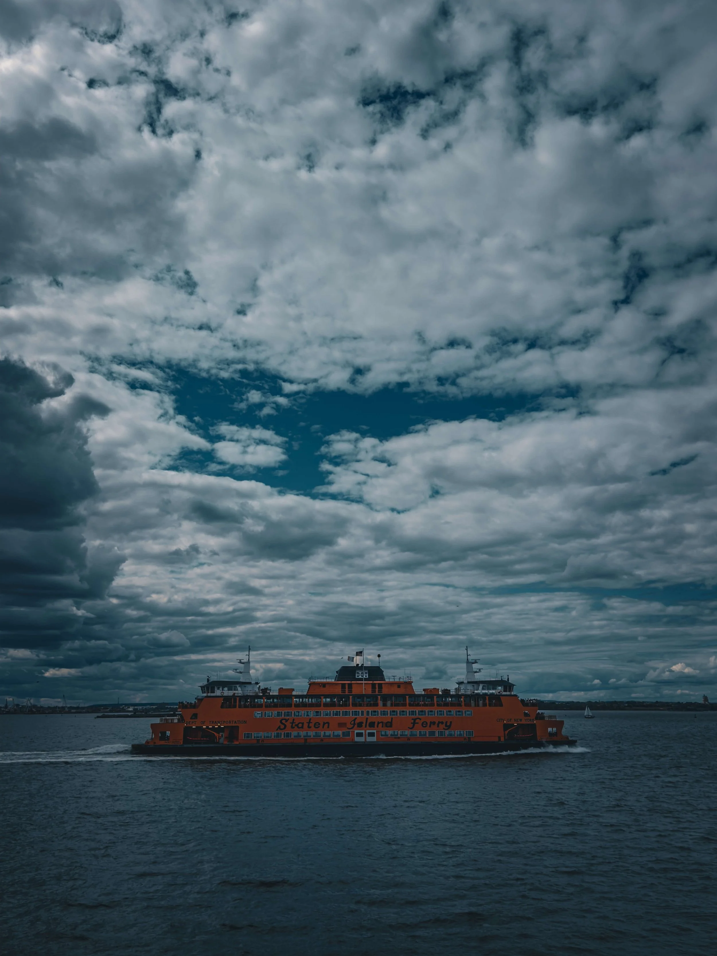 Orange Staten Island Ferryboat sailing on water under cloudy sky.