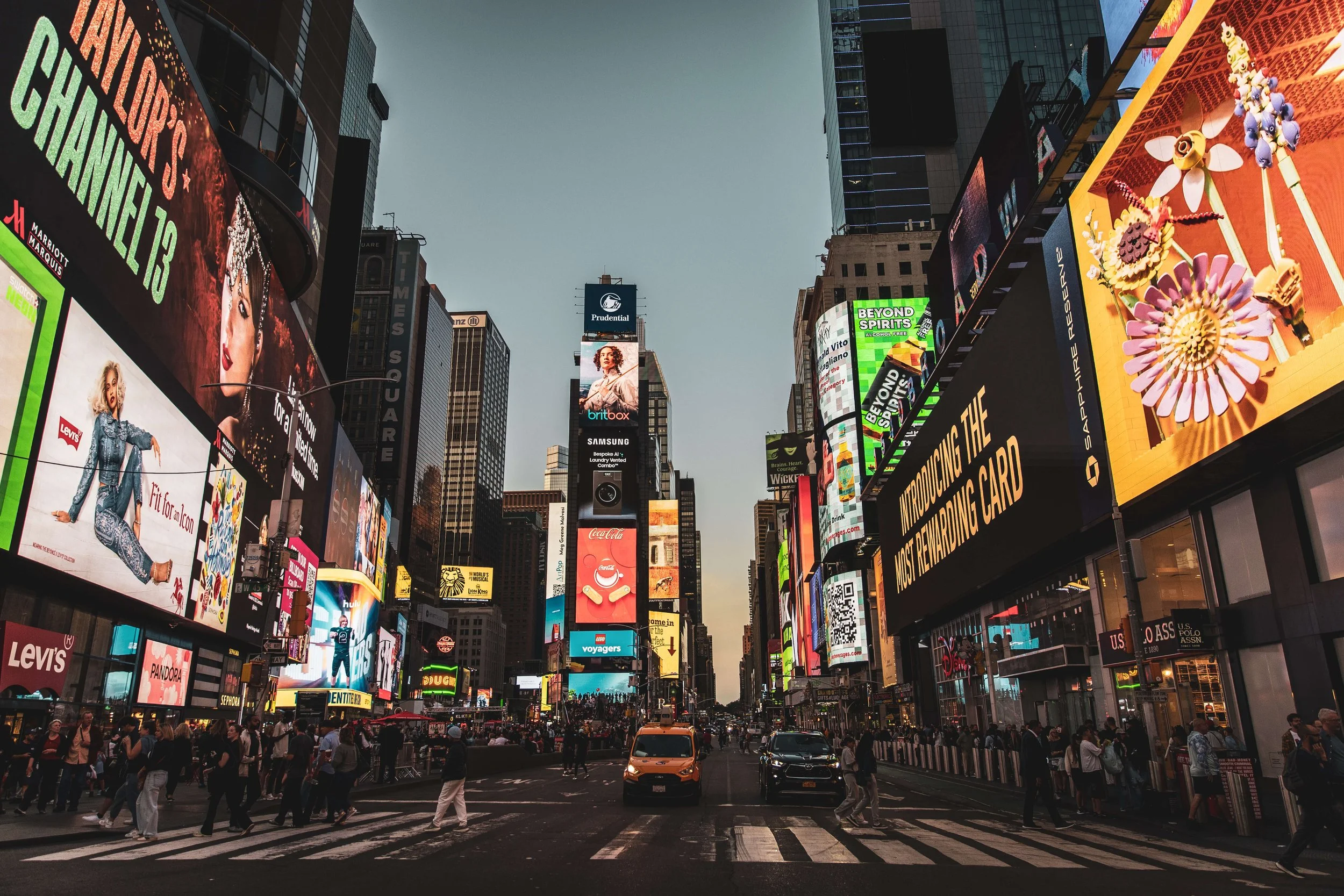 New York City Times Square with digital billboards, pedestrians crossing the street, and yellow taxi cabs.