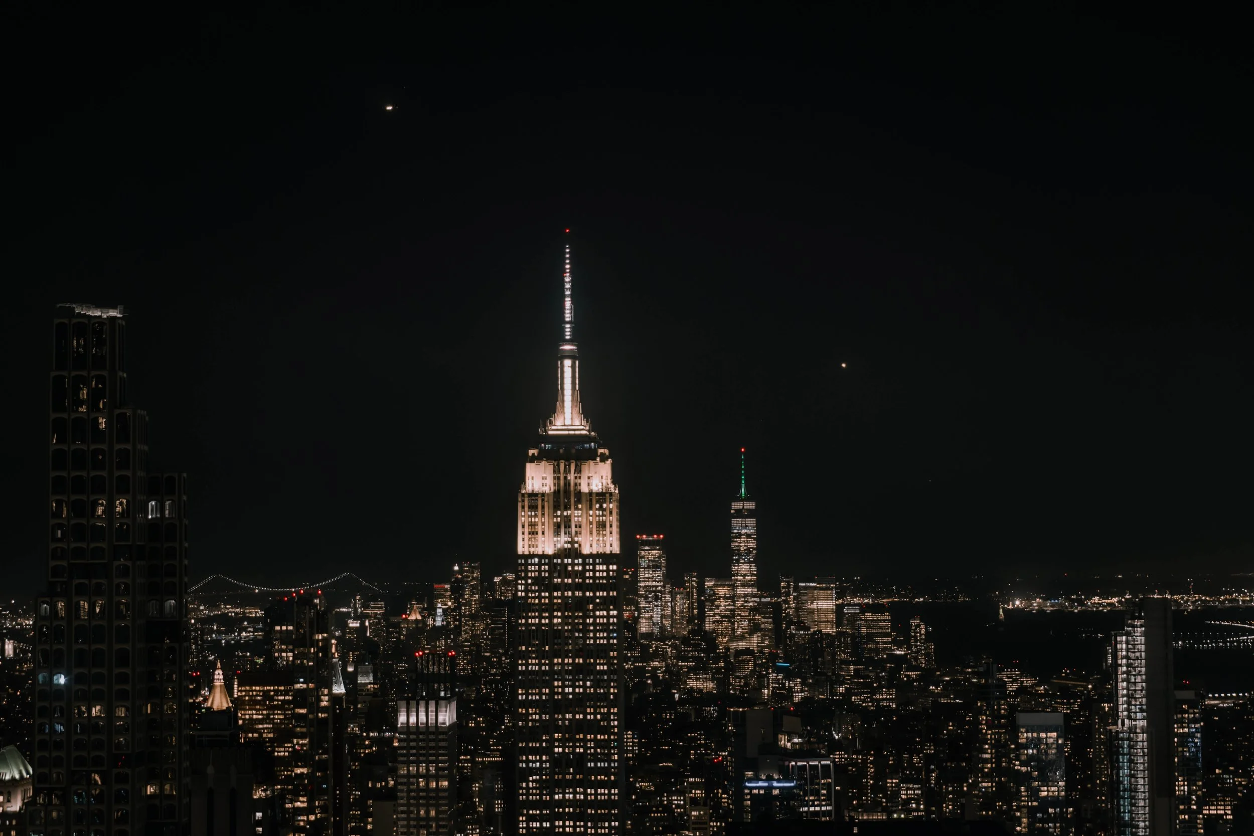 Nighttime cityscape of New York with the Empire State Building lit up and other city buildings illuminated.
