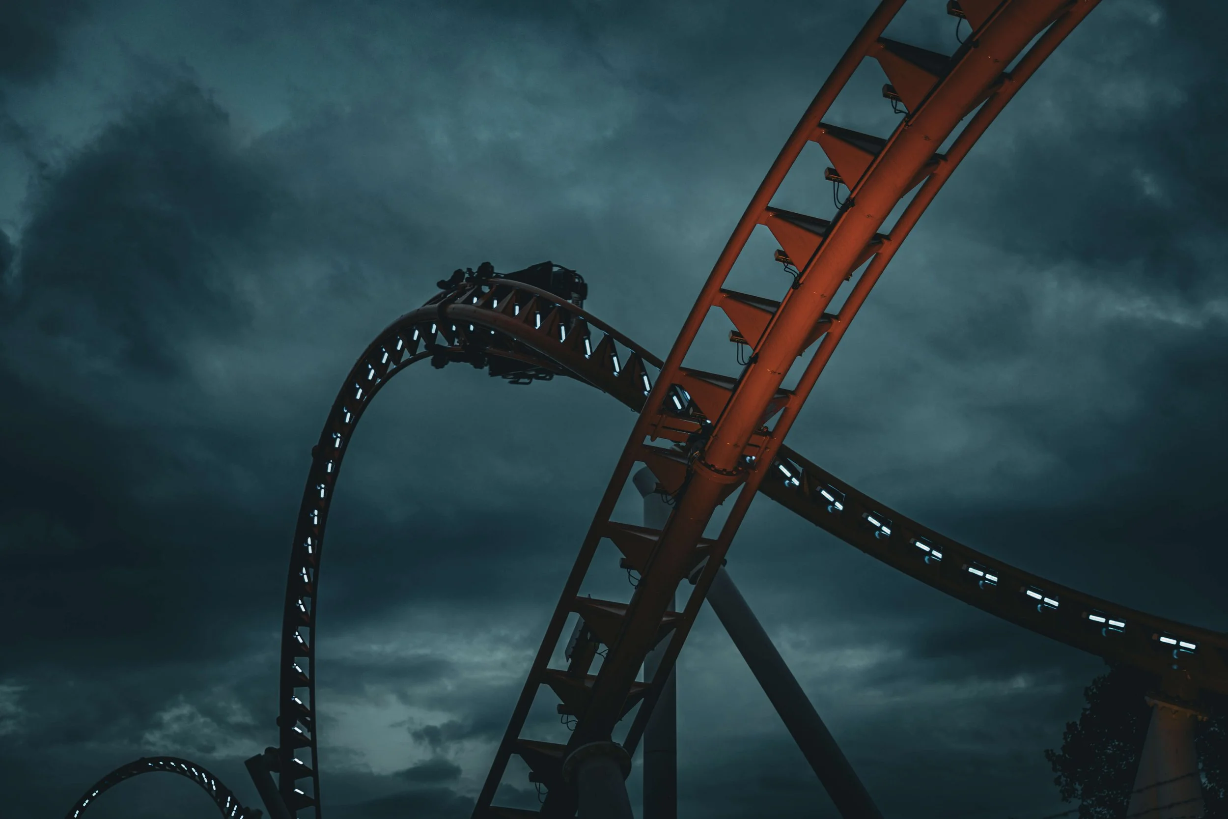 A dark photo of a roller coaster track against a cloudy sky at dusk.