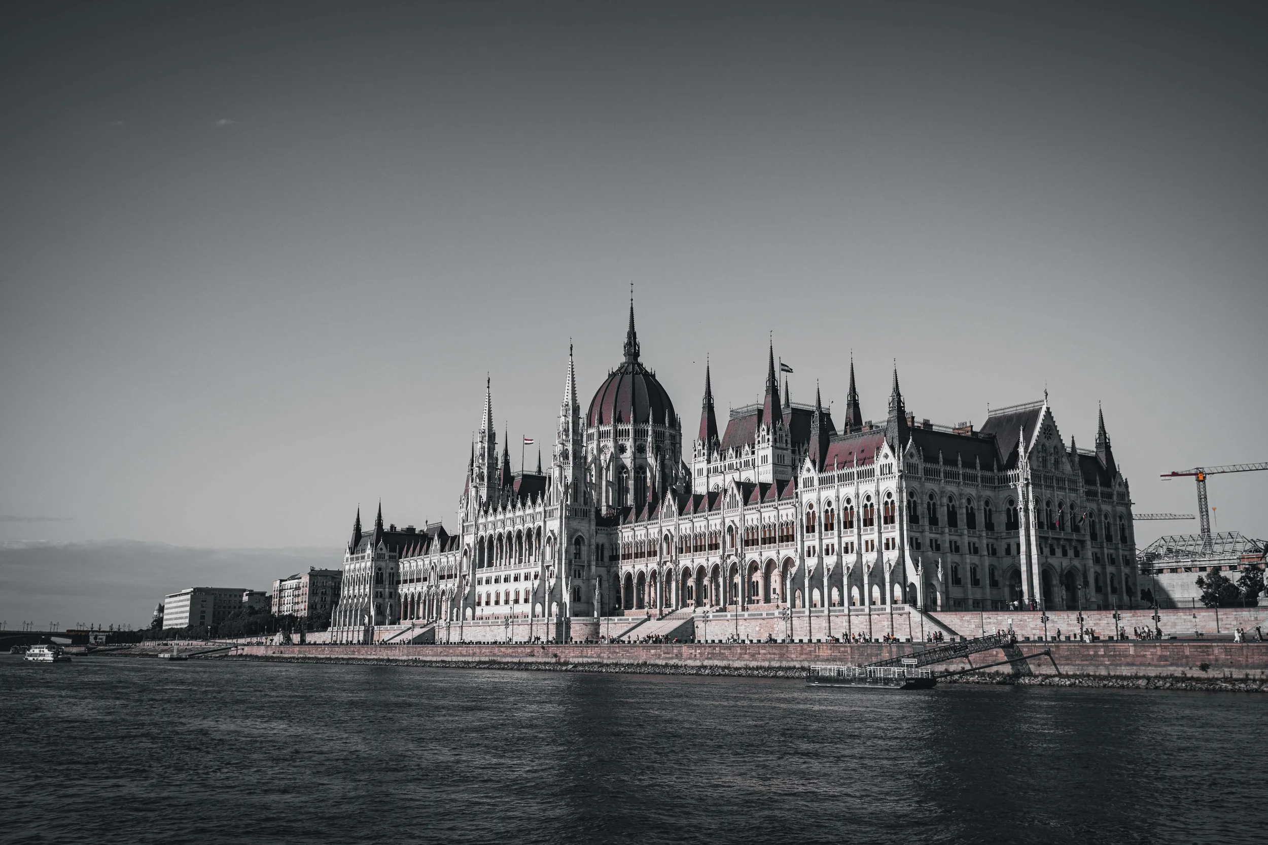 A grand historical building with pointed towers and ornate architecture along the riverbank, viewed from across the water.